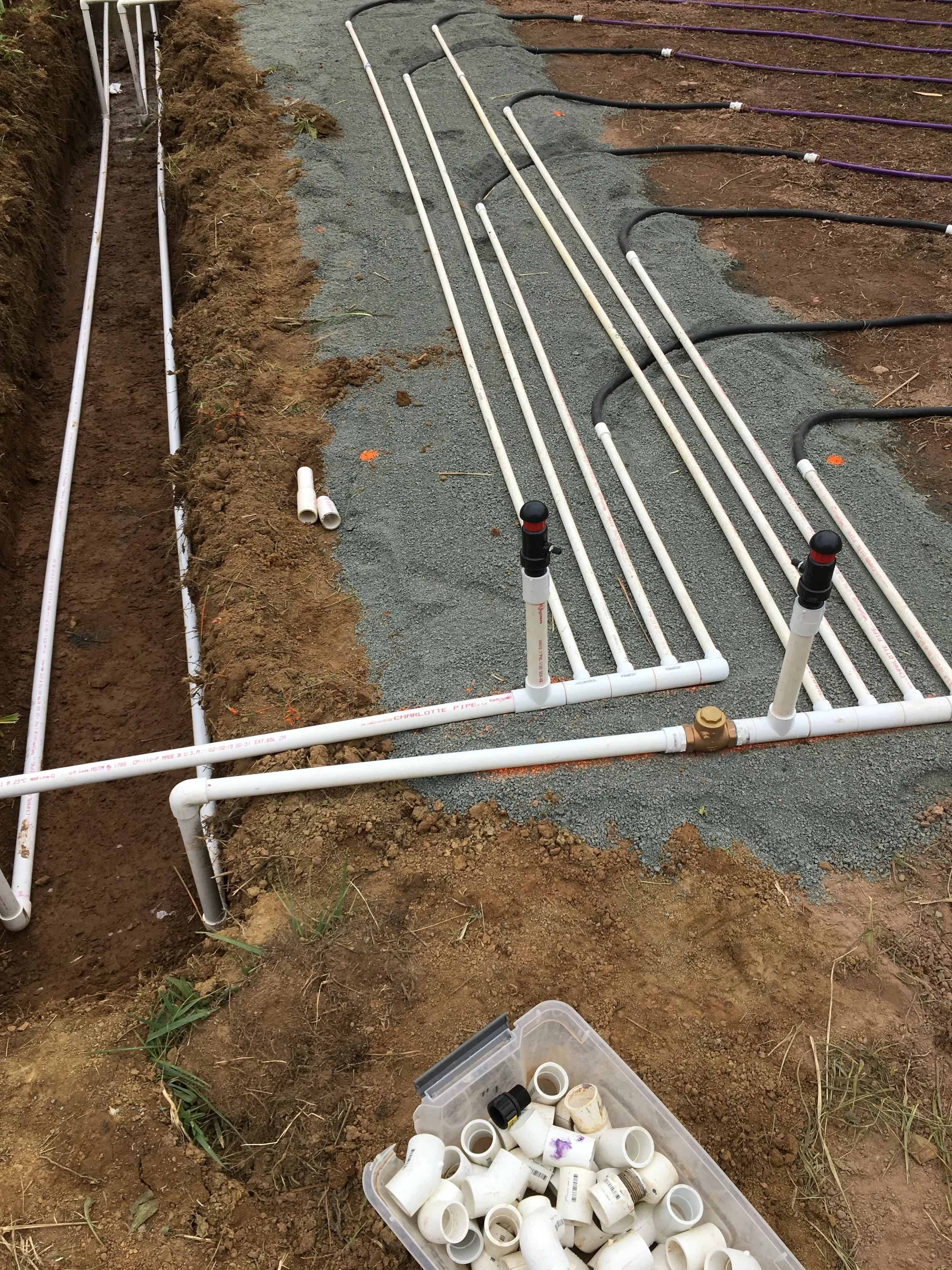 White PVC distribution manifold with control valves and black supply lines set on a gravel bed for a drip dispersal septic system in Northern Virginia.
