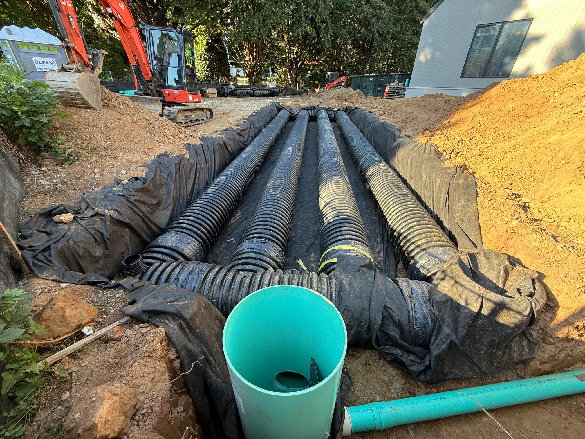 Corrugated HDPE stormwater detention pipes wrapped in geotextile fabric with taped joints and a riser connection in the foreground on a residential jobsite.