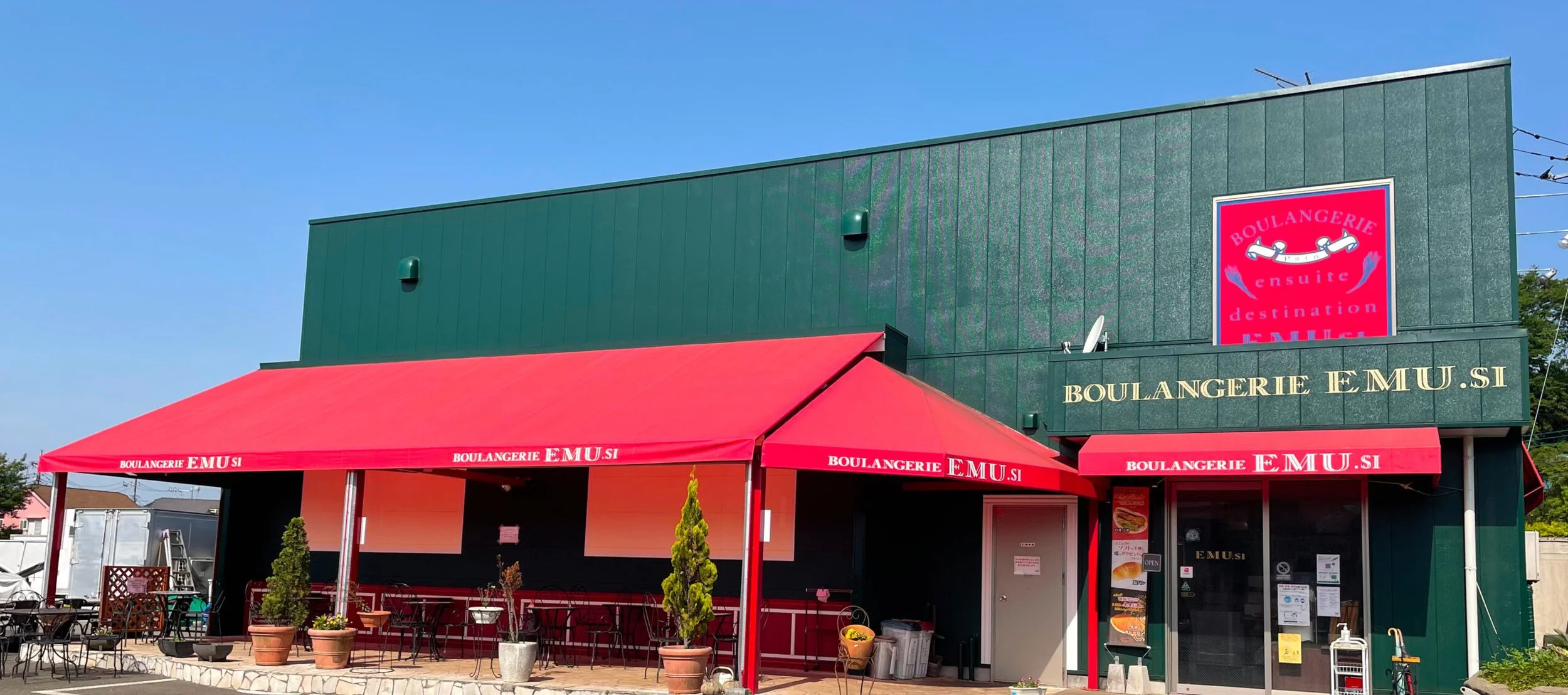 緑色の建物に赤いテントのパン屋さんの外観。看板には「BOULANGERIE EMU.SI」と書かれている。