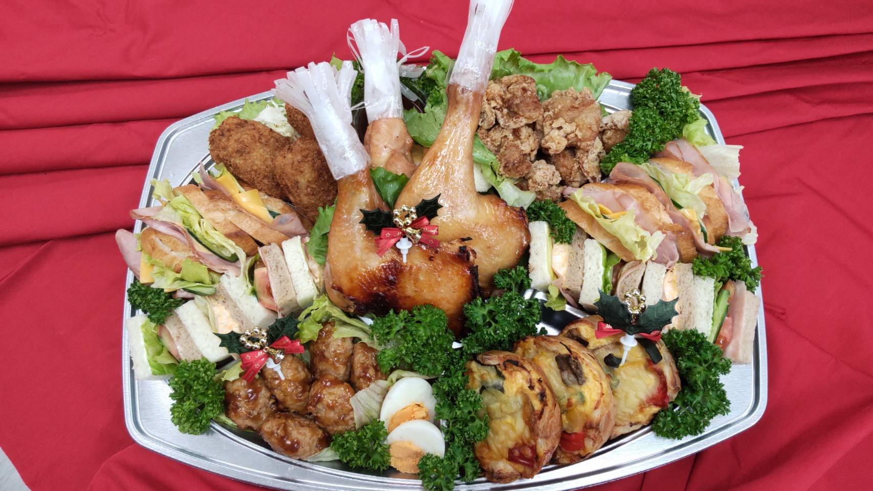 クリスマスの飾り付けがされたローストチキンの周りに一口サイズのサンドイッチ、唐揚げ、サラダ、ゆで卵などの料理が盛り付けられたクリスマス用の大皿料理。