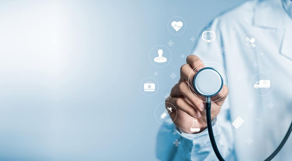 Healthcare professional holding a stethoscope with medical icons floating around, including a heart, heartbeat, bandage, medication, and ambulance.