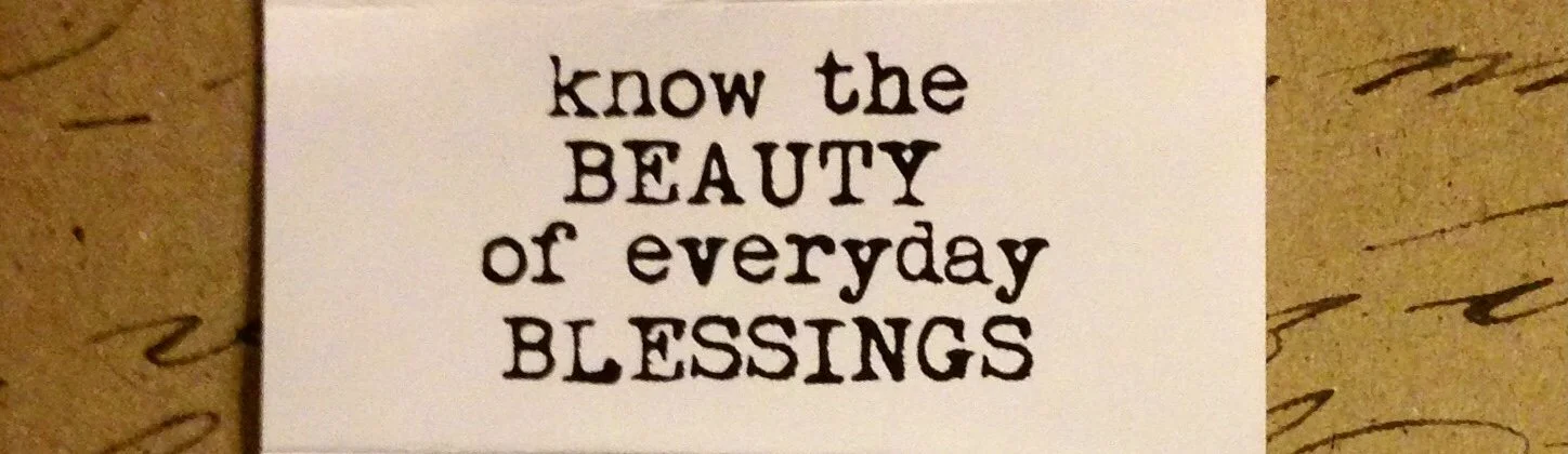 A white card with black printed text that reads "know the BEAUTY of everyday BLESSINGS." The card is placed on a wooden surface.