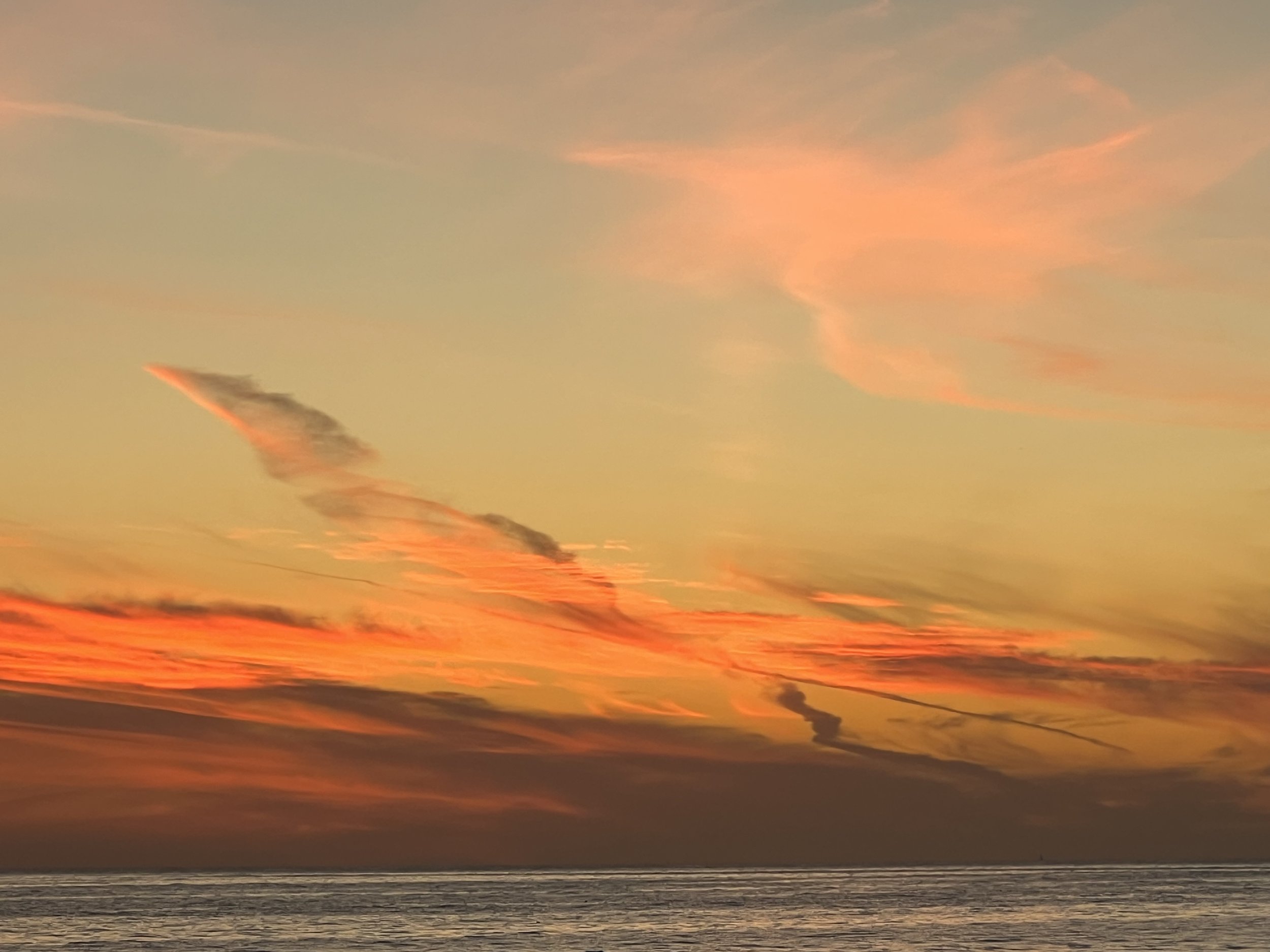 A sunset view over the ocean with vibrant orange and yellow clouds, and the silhouette of the seashore in the foreground.