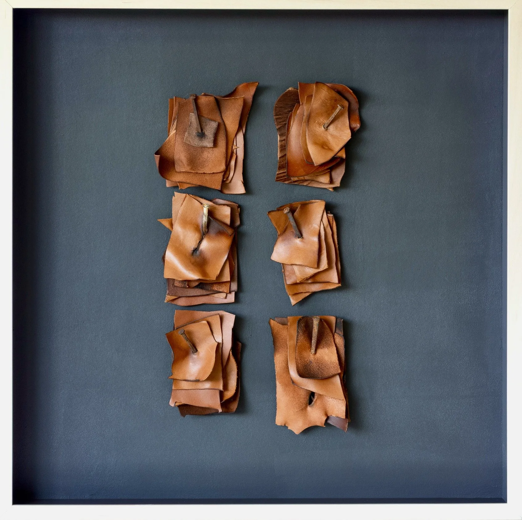 A framed display of vertically arranged brown leather pieces pinned to a dark gray background.