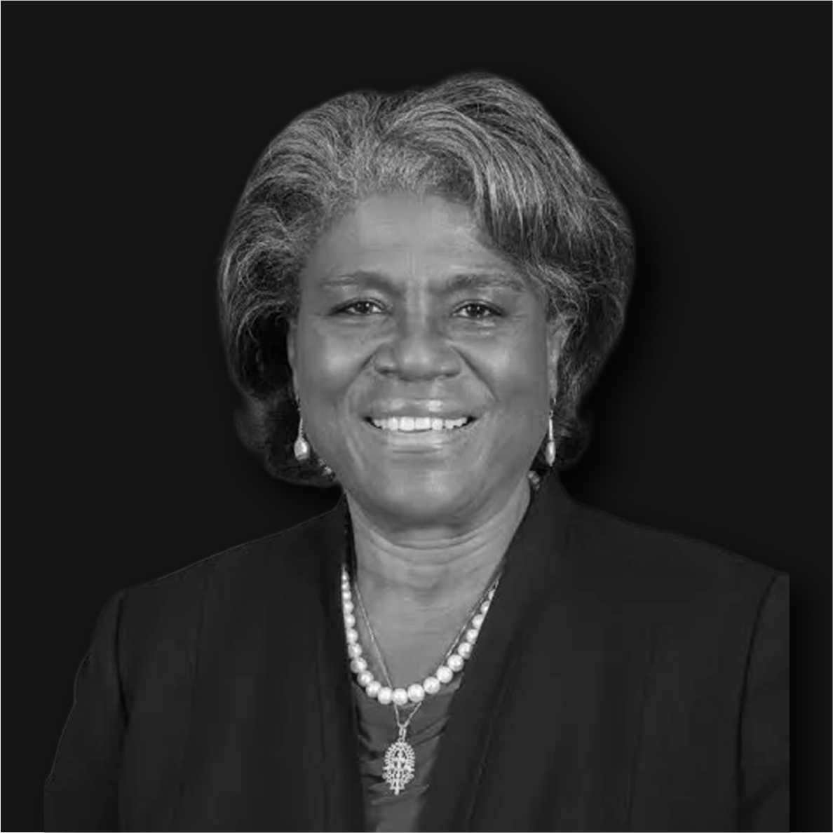 Black and white portrait of an older woman with gray hair, smiling, wearing earrings and necklaces, against a dark background.