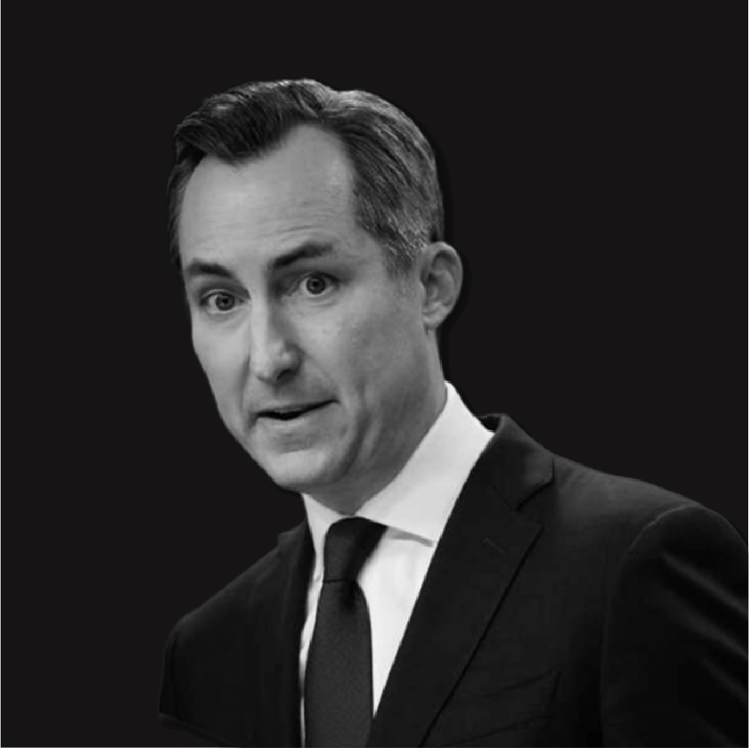 A black and white photo of a man in a suit and tie, with a neutral expression, against a dark background.