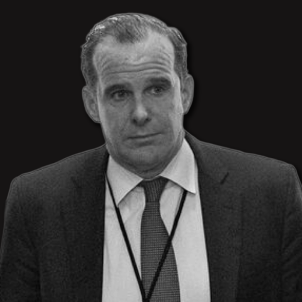Black and white photo of a man in a suit and tie, wearing a conference badge, against a dark background.