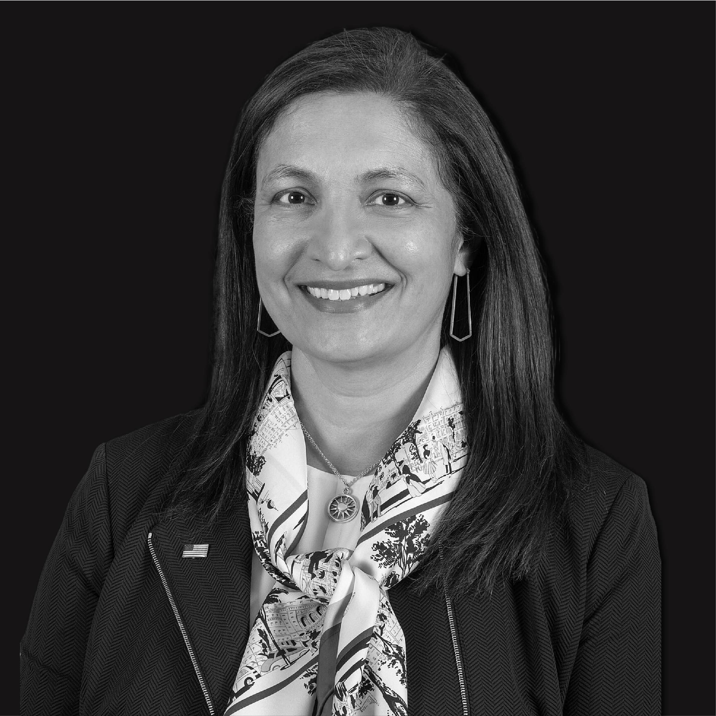 Black and white portrait of a smiling woman with long hair, wearing a patterned scarf, earrings, and a jacket against a dark background.