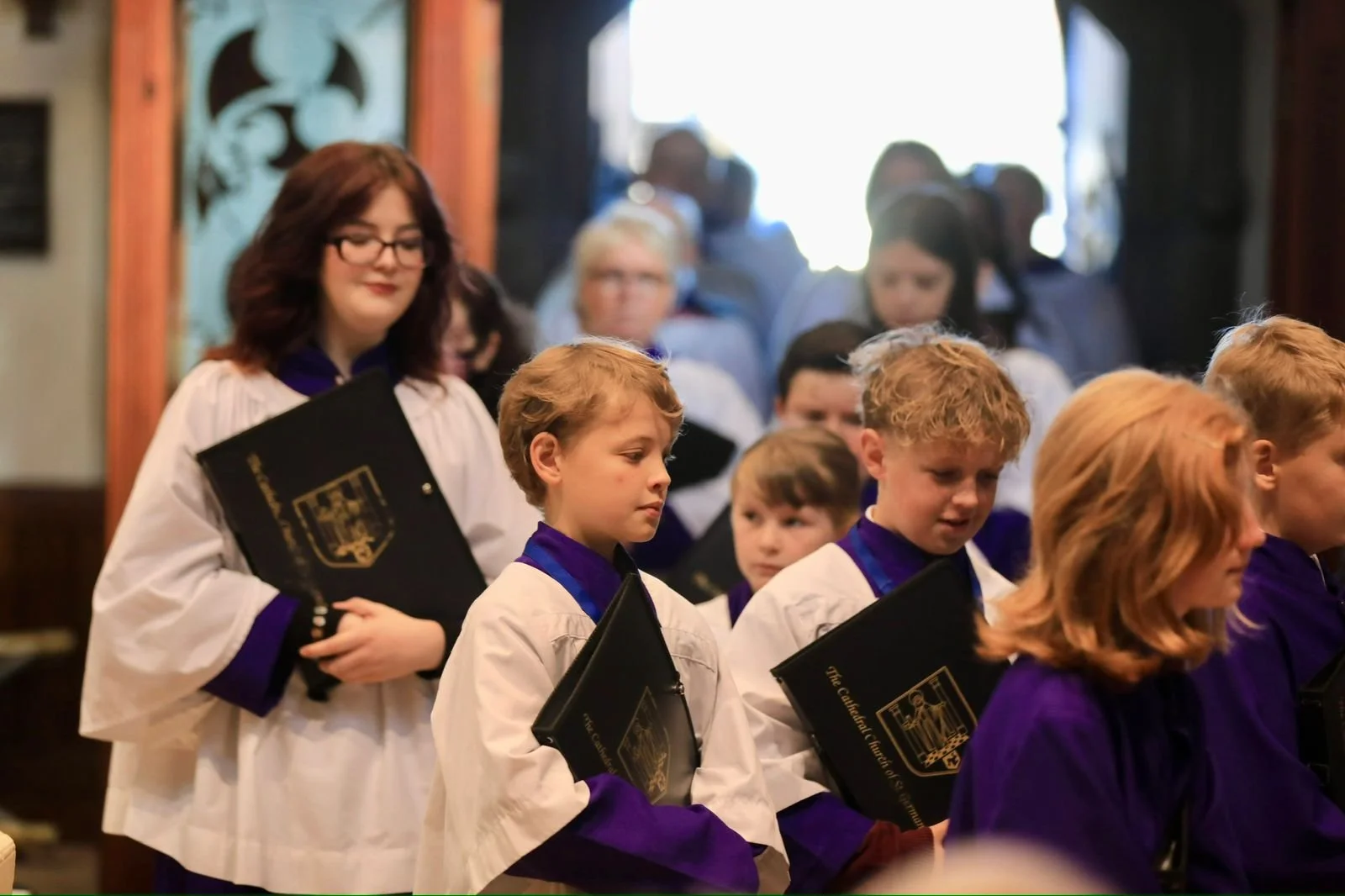 Children in choir robes holding sheet music processing during a church service.