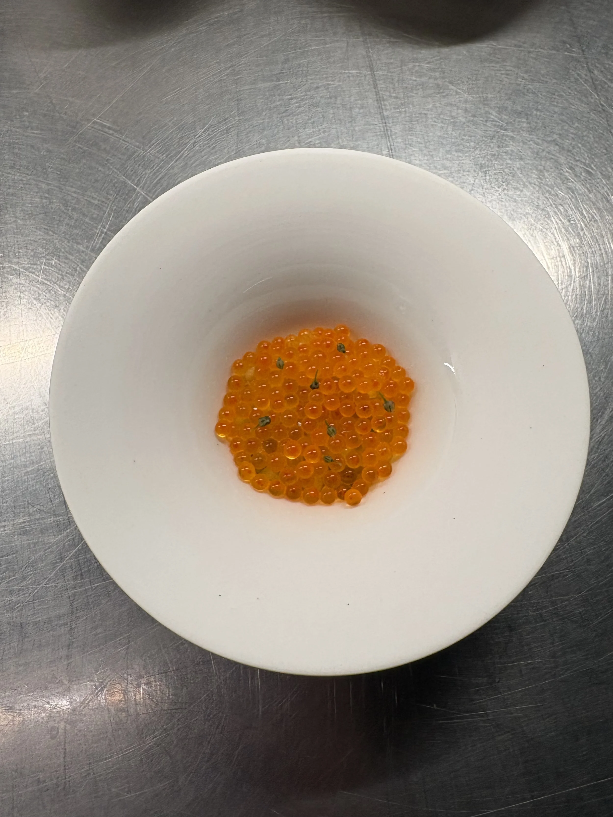 Orange fish roe in a white bowl on a metal countertop.