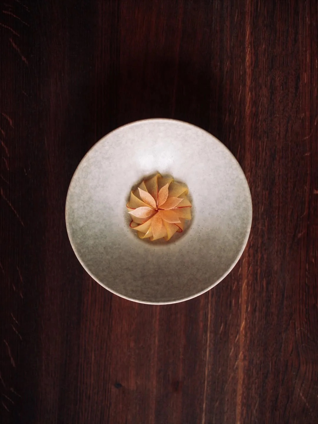 A small wrapped flower-shaped gift on a white plate placed on a dark wooden table.