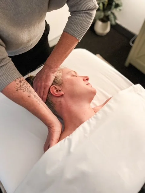 A person receiving a massage on her neck and head while lying in bed.