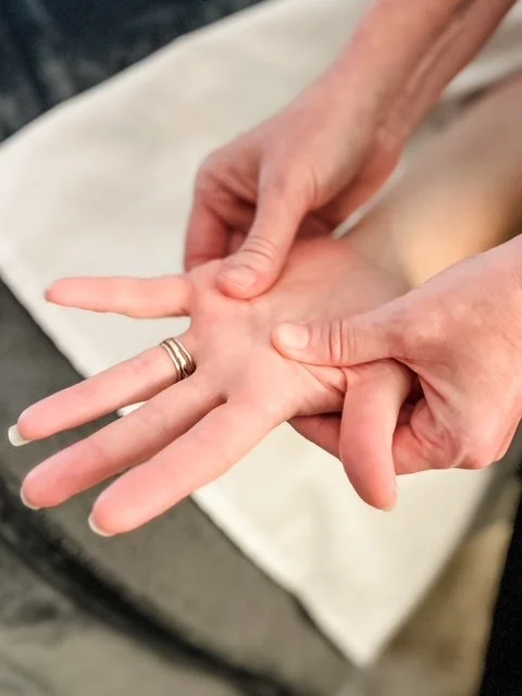 Person receiving a hand massage or therapy, with a therapist pressing on the palm of their hand.