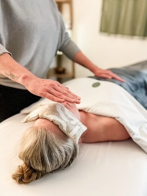 Person performing reiki on an woman lying on a massage bed.