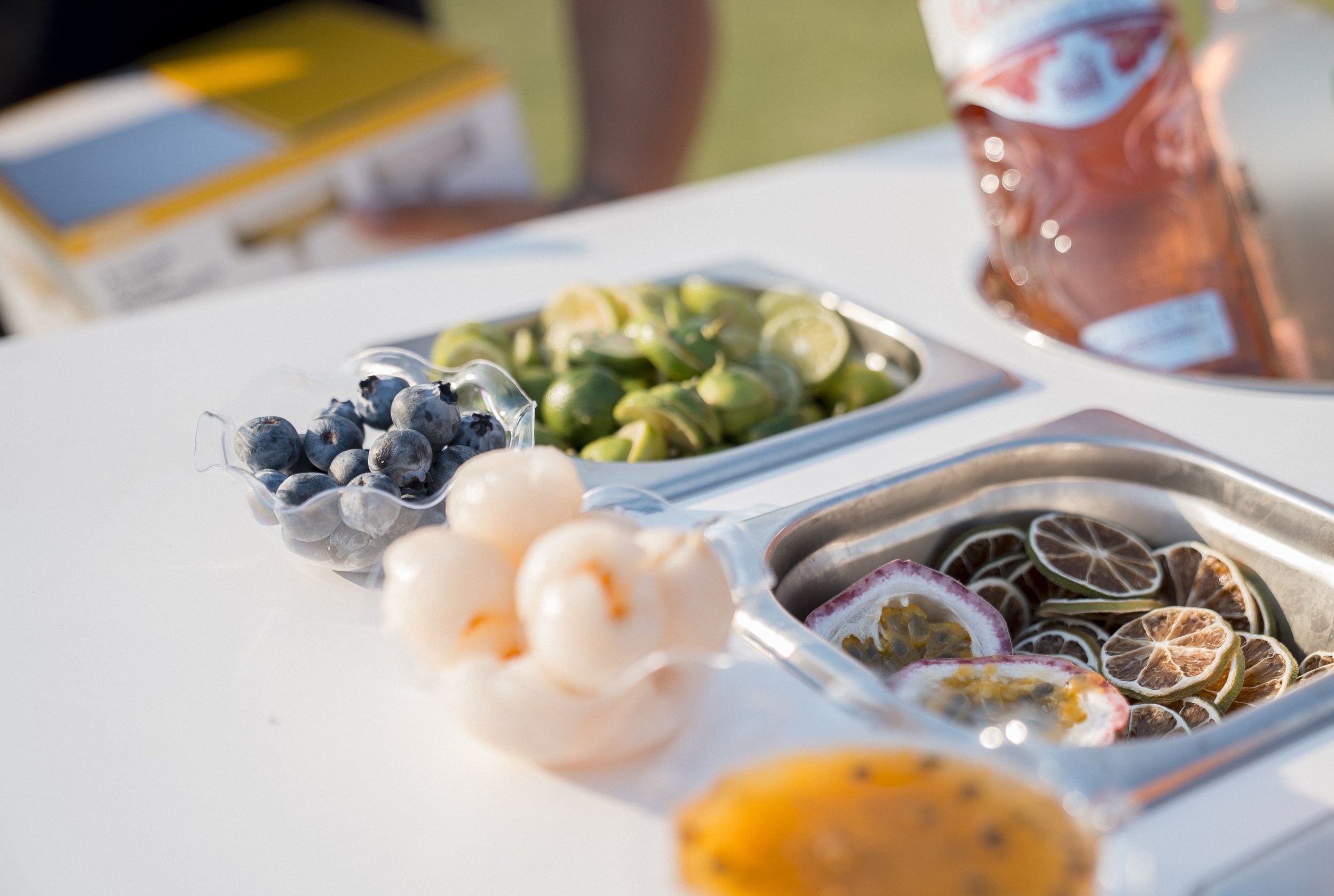 Close-up of a tray of sliced citrus fruits and small bowls of fresh blueberries and other fruits at an outdoor event.