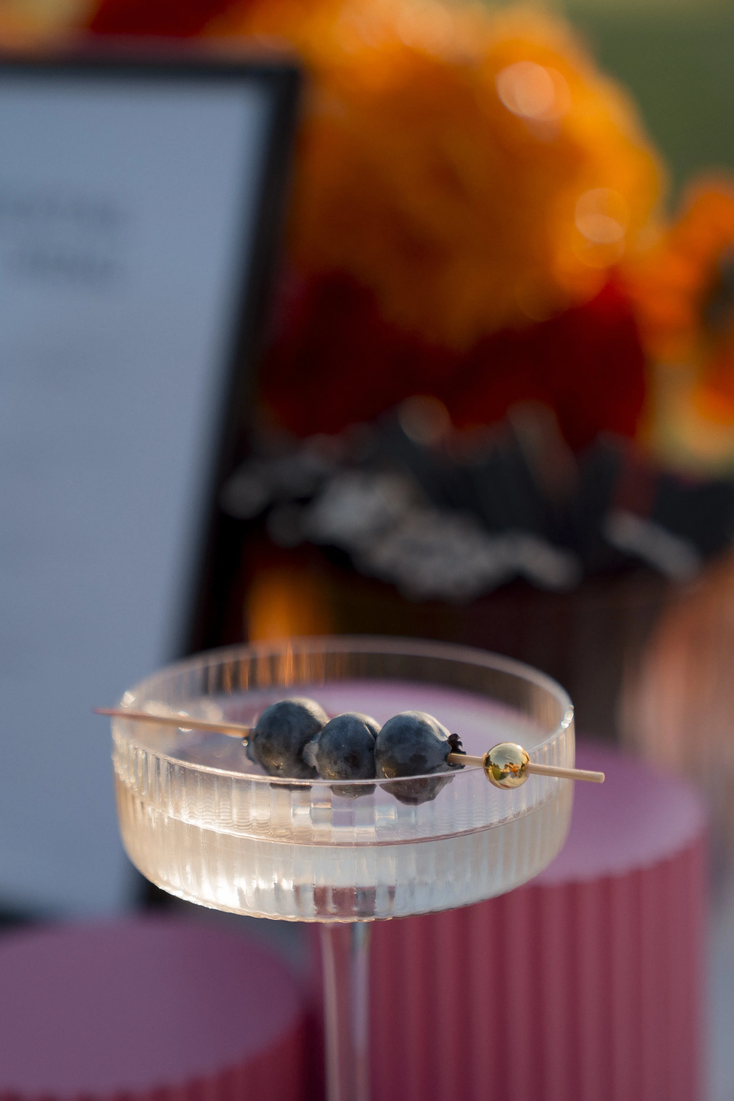 A glass of blueberries on a stick with a gold bead, with blurred autumn leaves in the background.