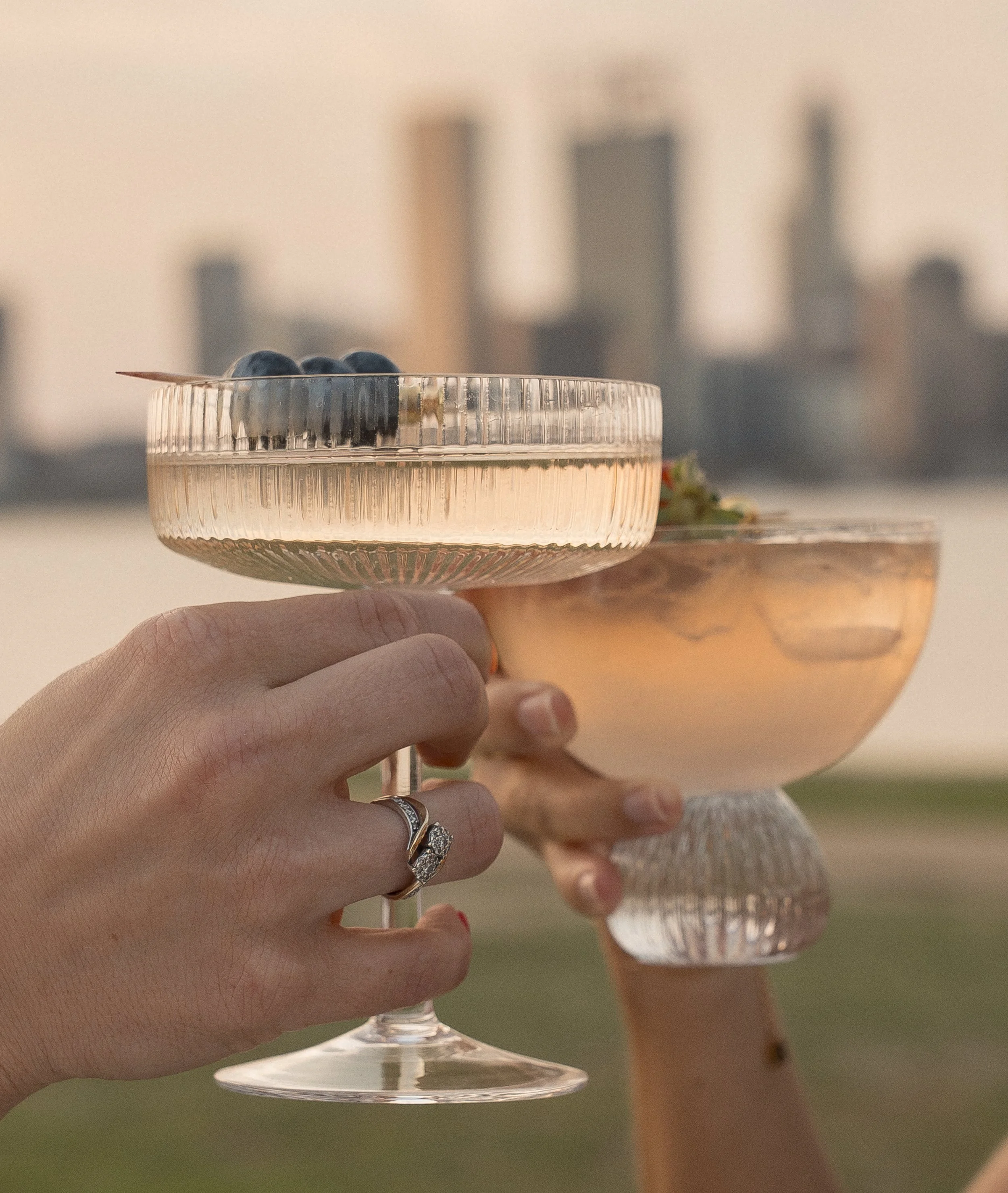 Two women holding glasses of champagne and a tray with blueberries at an outdoor event during sunset.