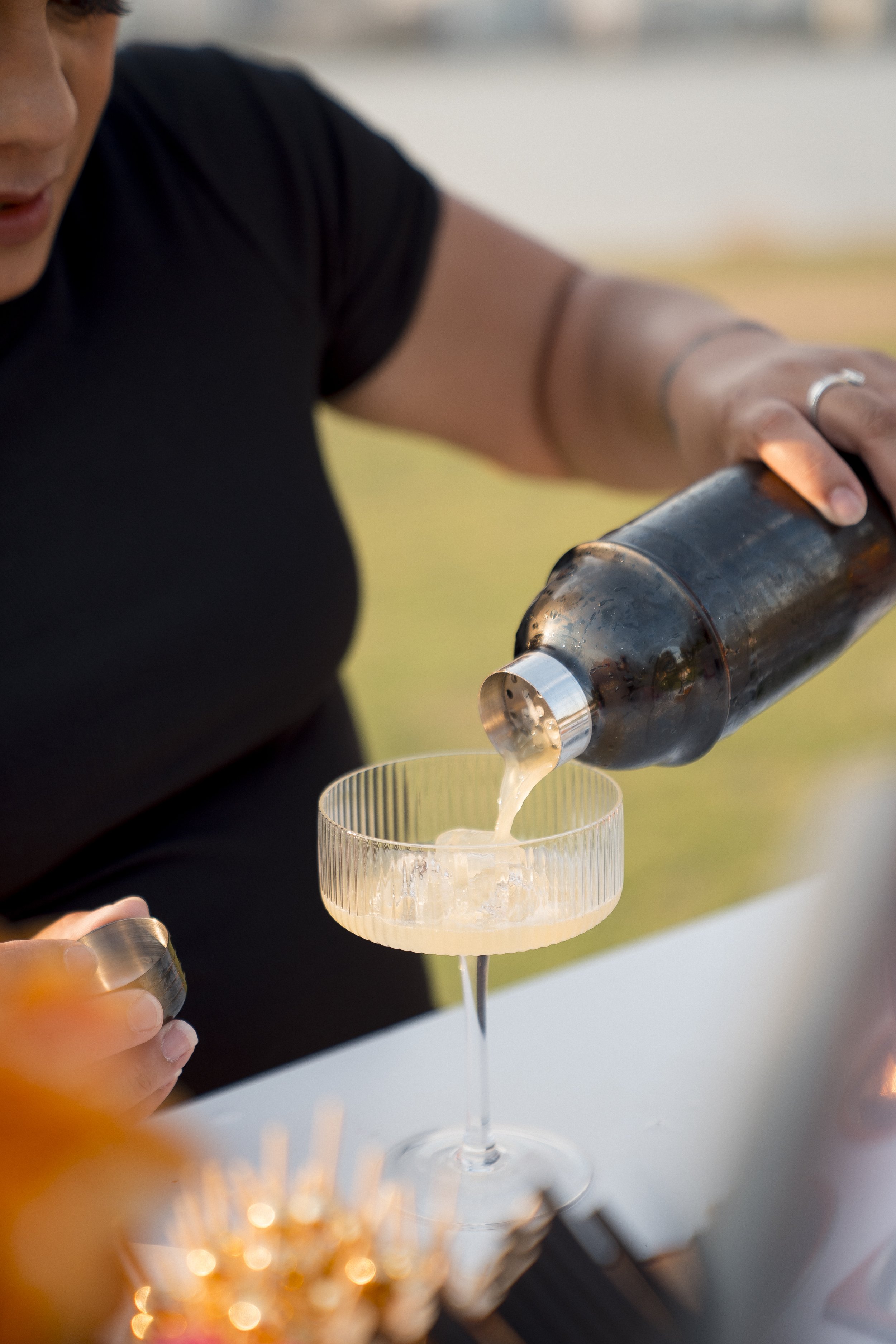 Person pouring a drink from a bottle into a glass with ice. The setting appears to be outdoors, possibly a celebration or gathering.