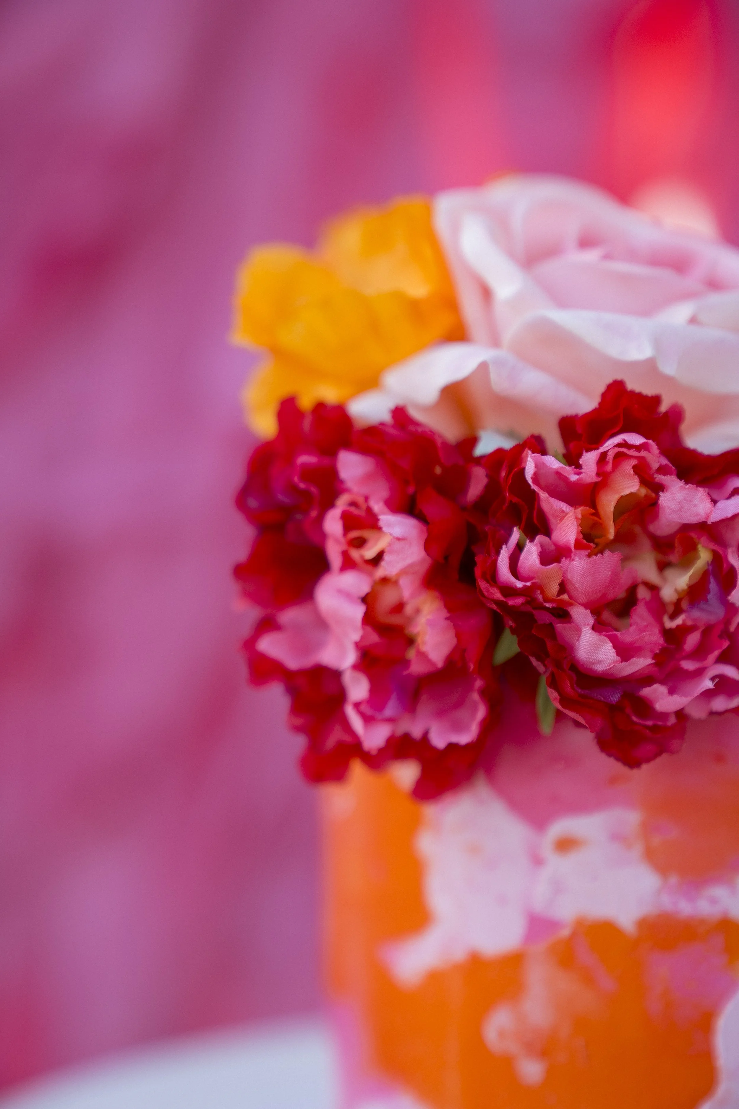 Close-up of pink, white, red, and orange carnations with blurred pink, orange, and purple background.