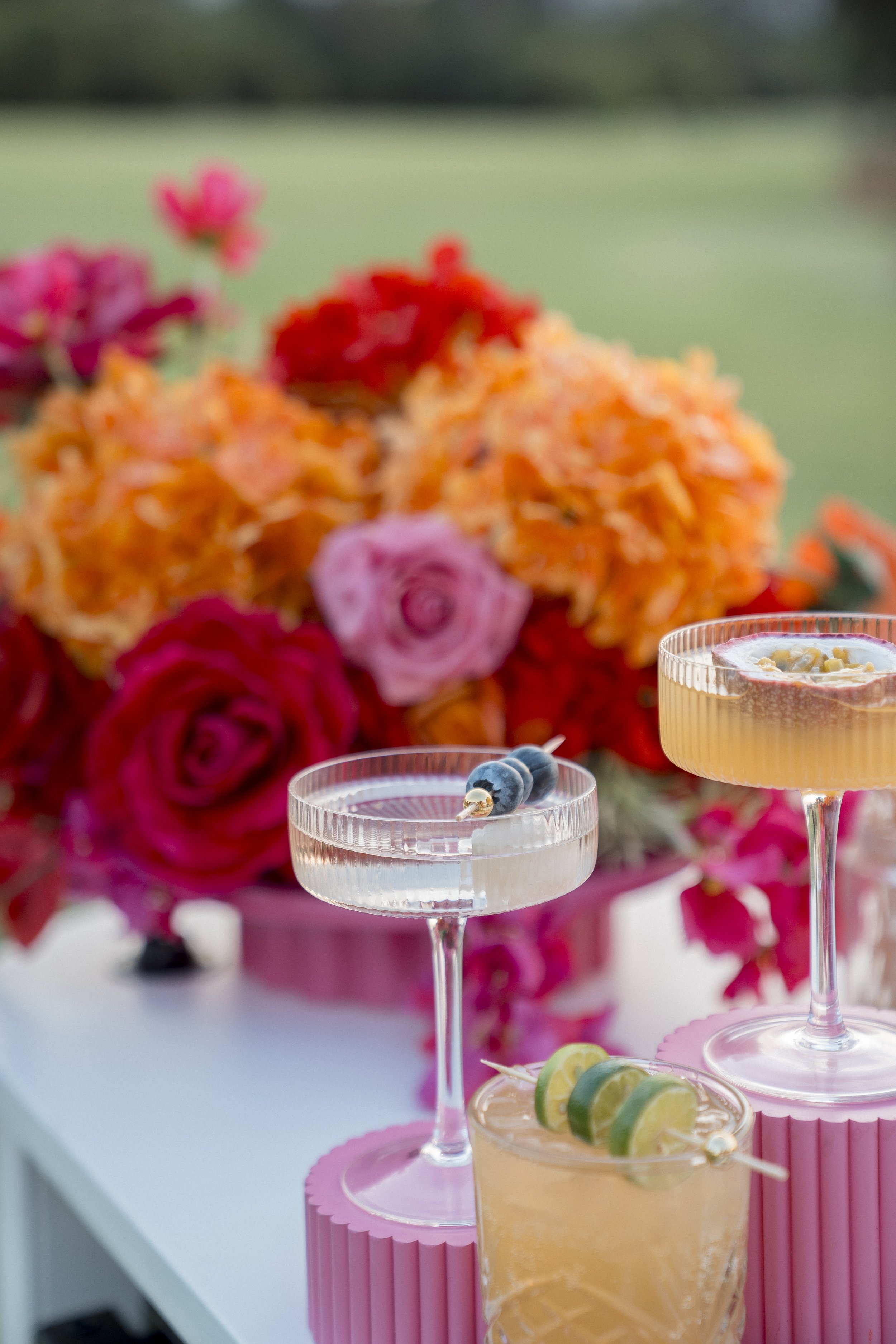Colorful desert cocktails on a table with a background of vibrant flower arrangements.