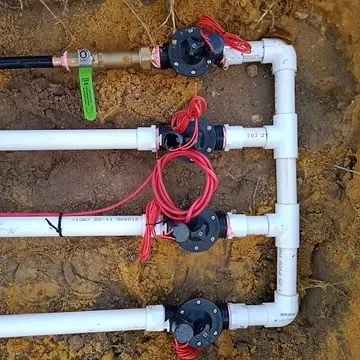 Pipeline with black valve handles, red strings, and white PVC pipes in a dirt trench.