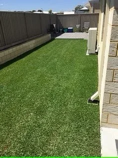 A backyard with a well-maintained green lawn, enclosed by a wooden fence, with a small patio area at the far end.