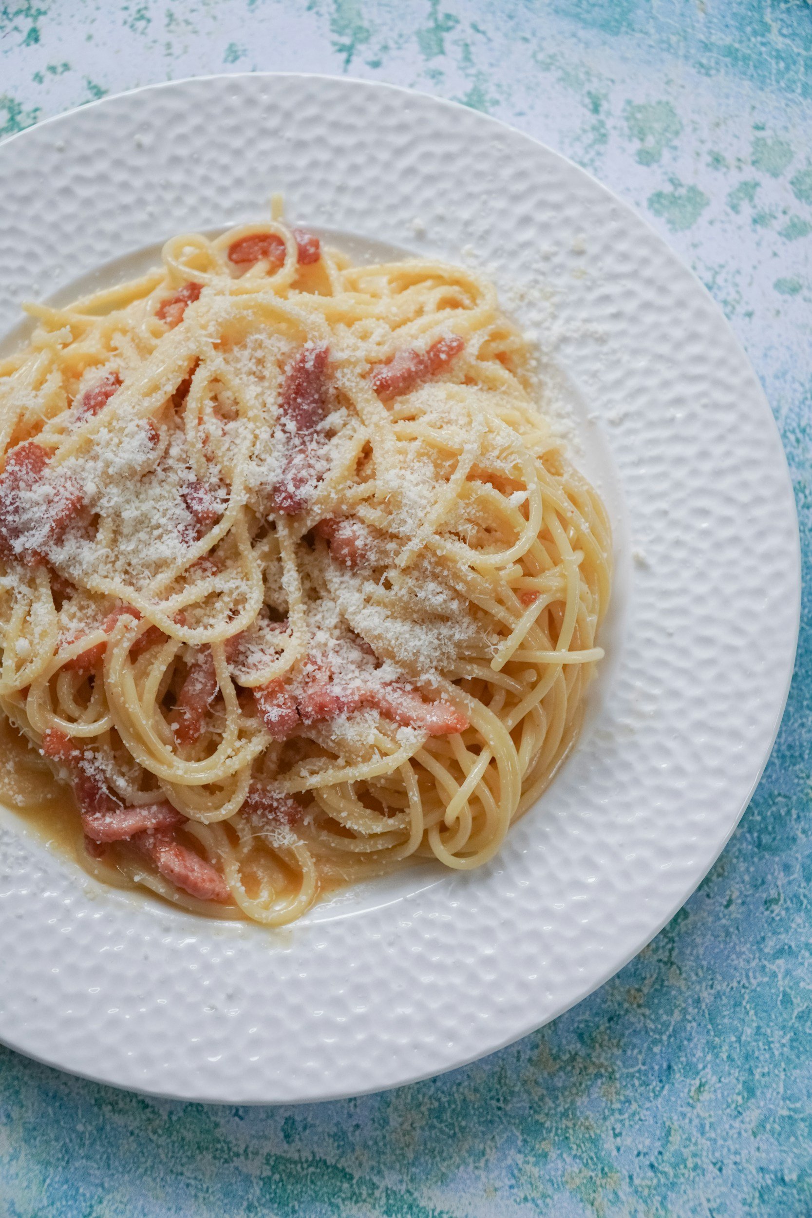 Piatti di spaghetti con pomodoro e formaggio grattugiato, serviti in un piatto bianco decorato.