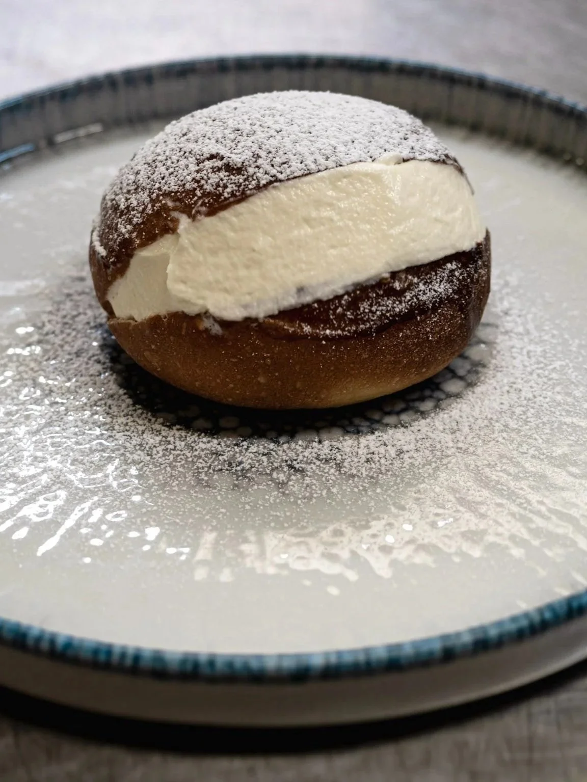 Pasticcino con cioccolato fondente, crema e polvere di zucchero a velo, disposto su un piatto.
