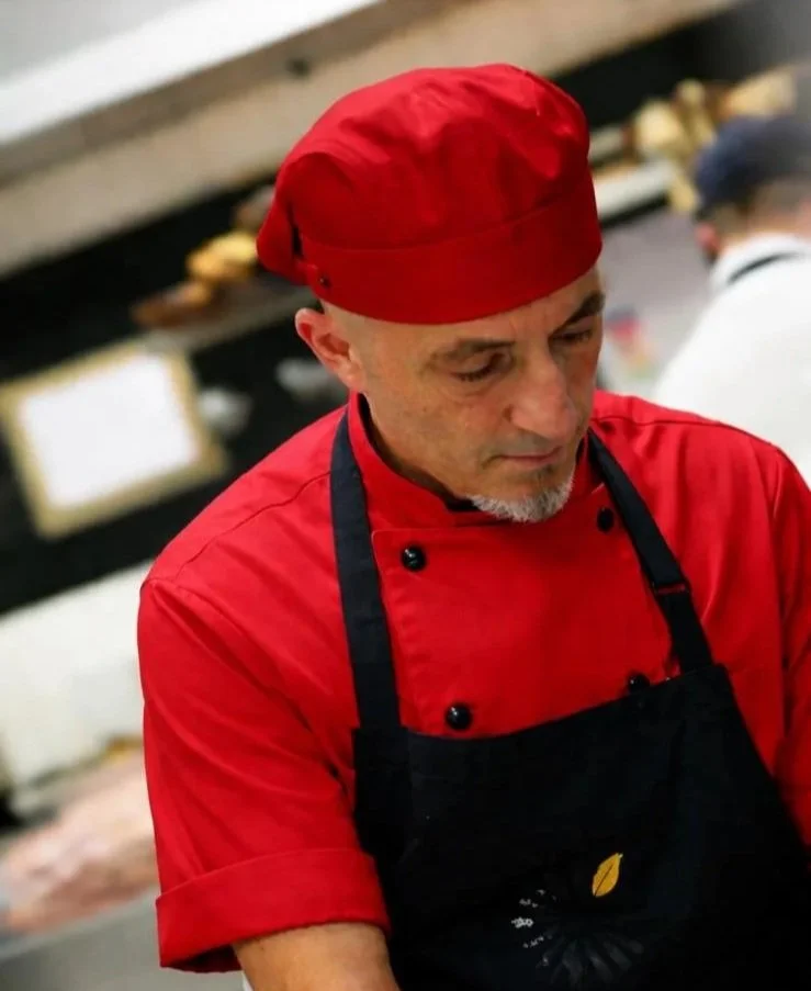 Un uomo chef con cappello e grembiule rossi, concentrato mentre cucina in una cucina professionale.