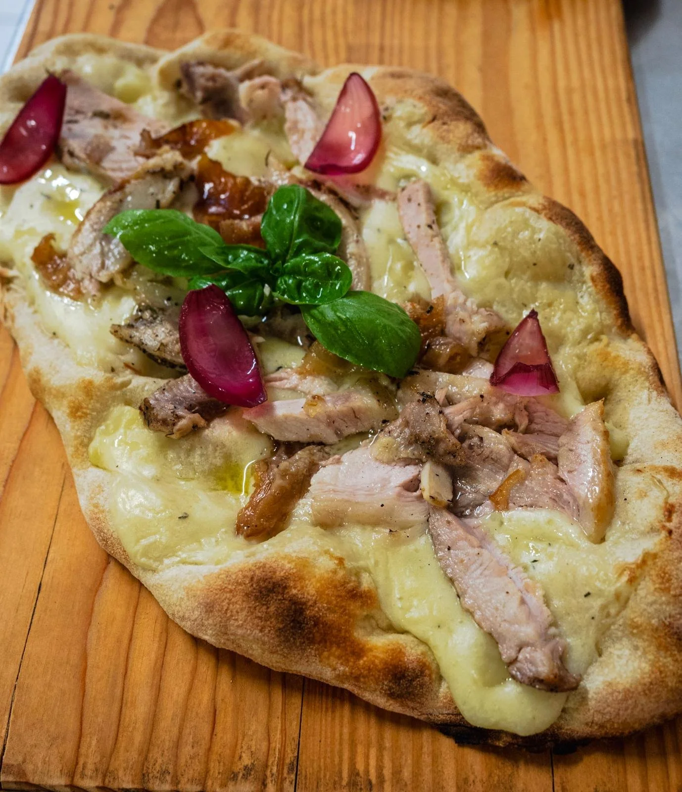 Pizza con prosciutto, formaggio, basilico e cipolla rossa su una crosta spessa, servita su un tagliere di legno.