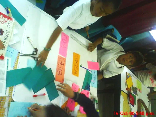 Niños trabajando en un proyecto escolar con papel de colores en una mesa.