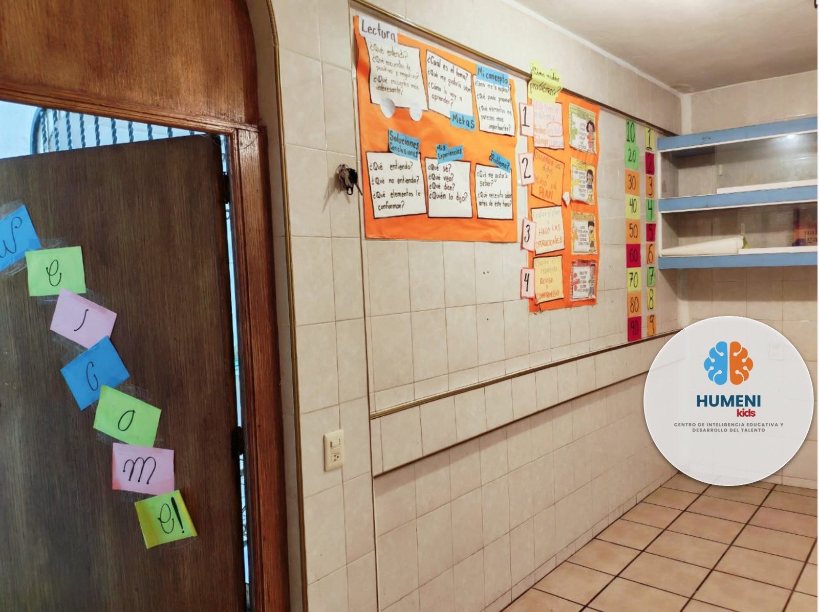 Cartel en la pared con información educativa sobre lectura, formas de entender y soluciones, decorado con notas y dibujos. Estantes vacíos a la derecha y pared con números del 10 al 90 en colores diferentes. En la esquina inferior derecha, logotipo d