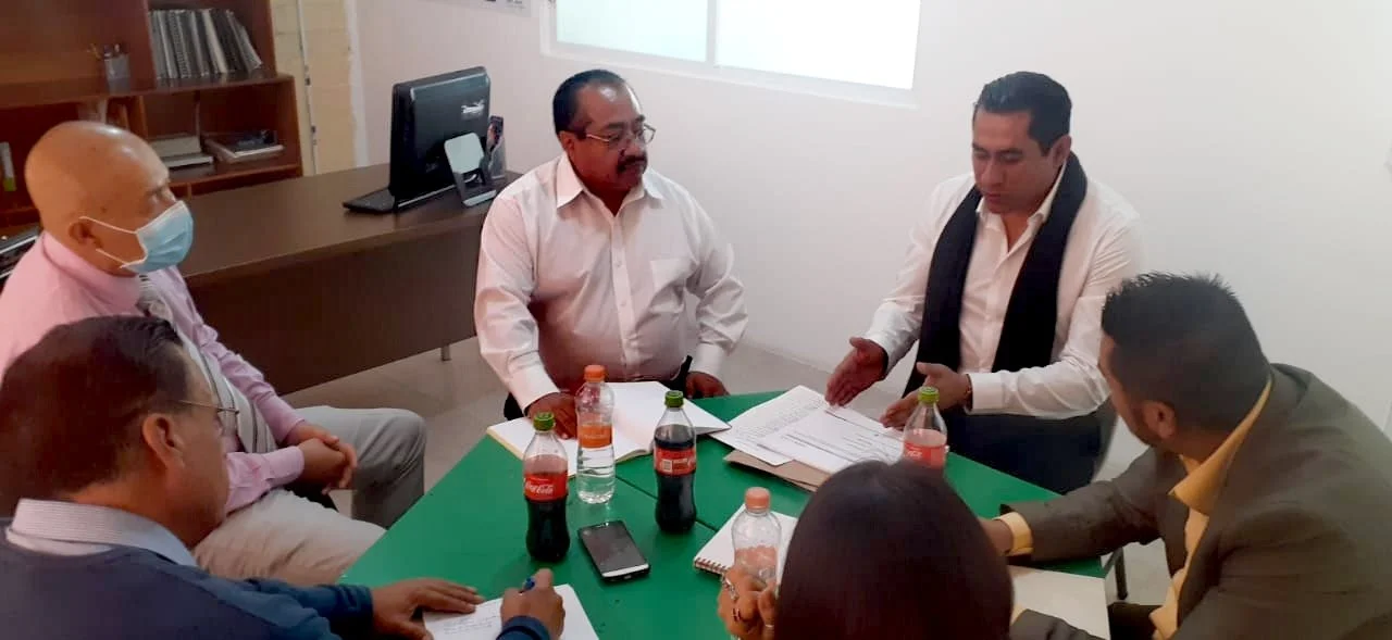 Grupo de seis personas en una reunión en una oficina, con documentos y botellas de refresco en la mesa.