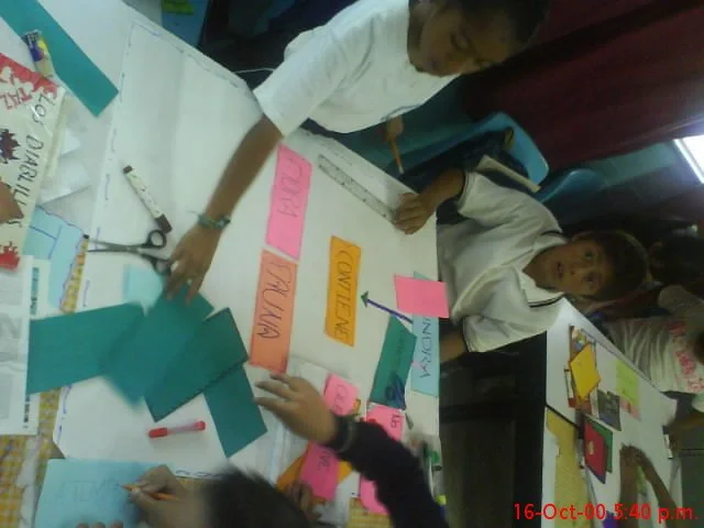 Niños en un aula participando en una actividad con tarjetas y papeles de colores sobre una mesa.