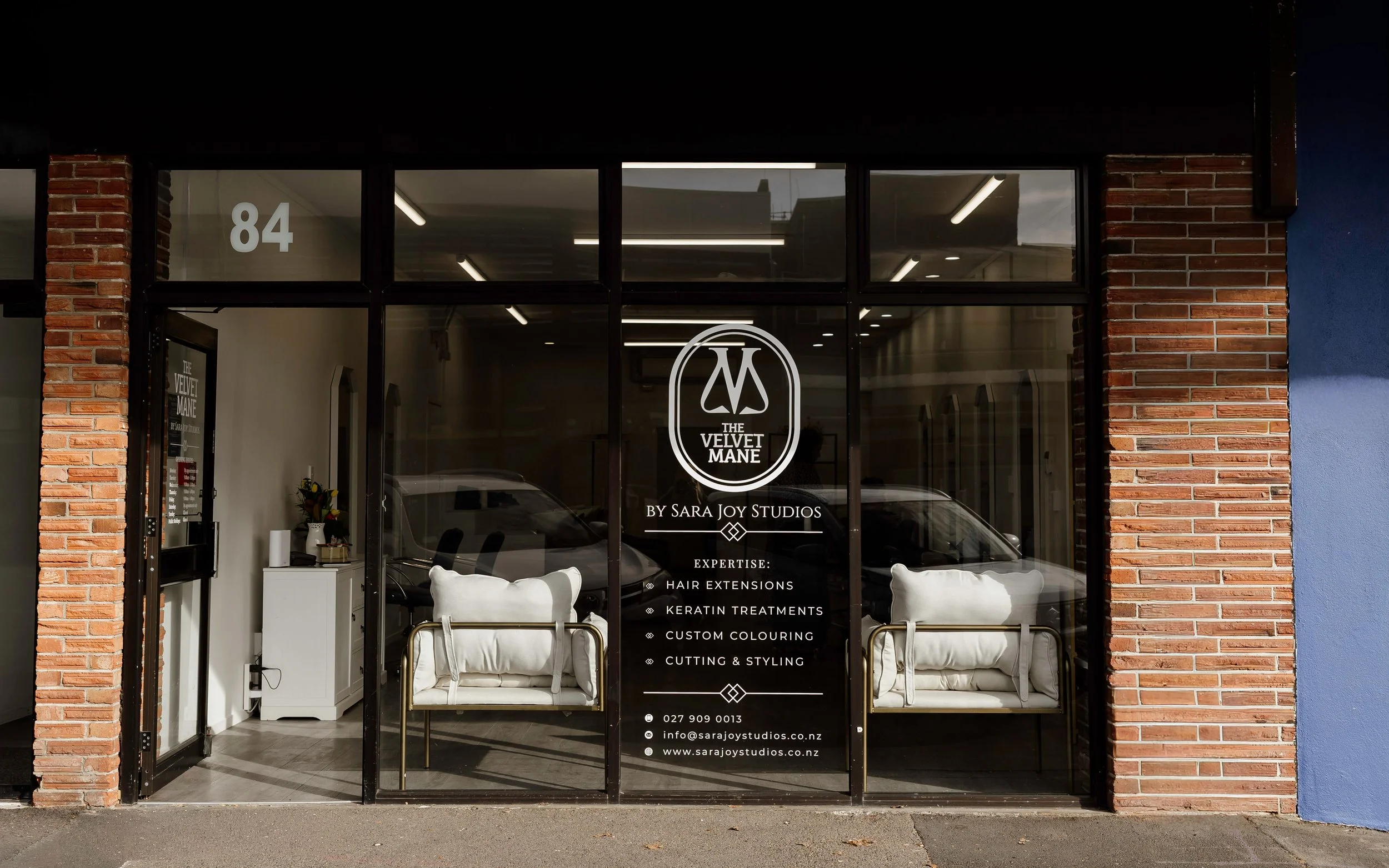storefront with glass doors and windows, brick accents, and a sign for 'The Velvet Mane by Sara Joy Studios' offering hair extensions, keratin treatments, and styling services.