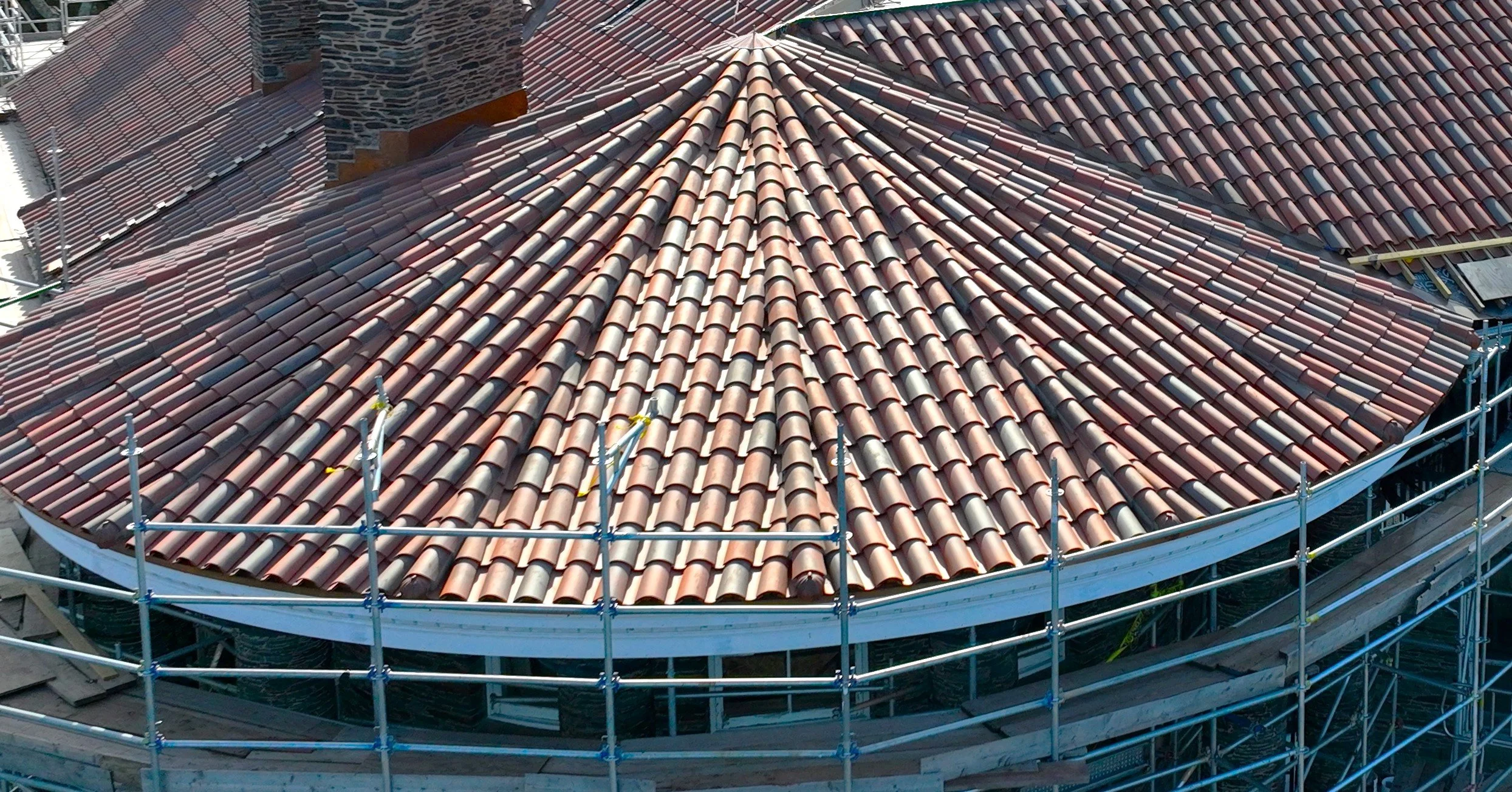 View of a rooftop with red clay tiles under construction, surrounded by metal scaffolding.