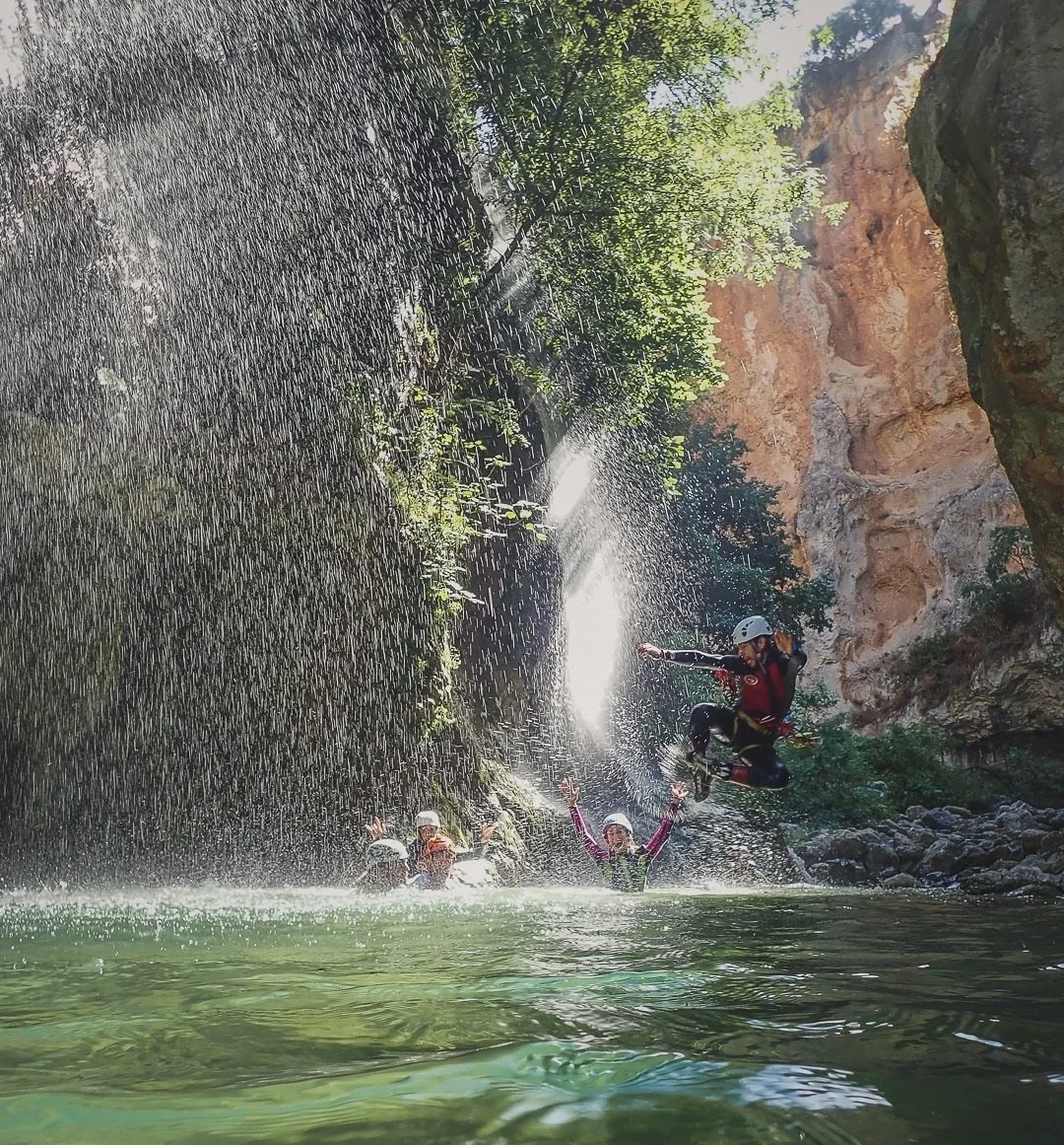 Personas practicando rappel en una cascada de agua en un entorno natural con rocas, árboles y paredes de piedra.