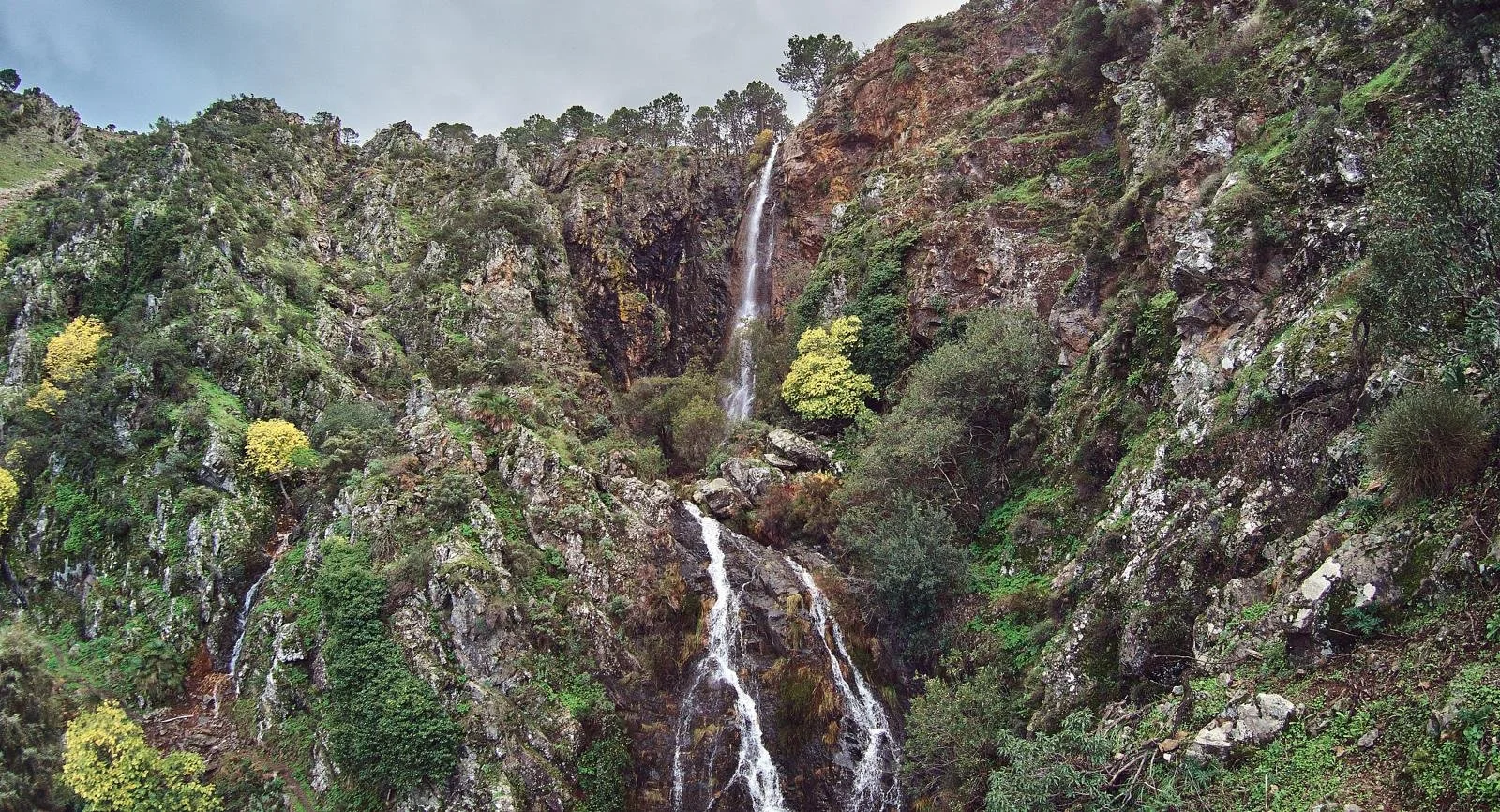 Cascada en una zona de montañas verdes con rocas y árboles.