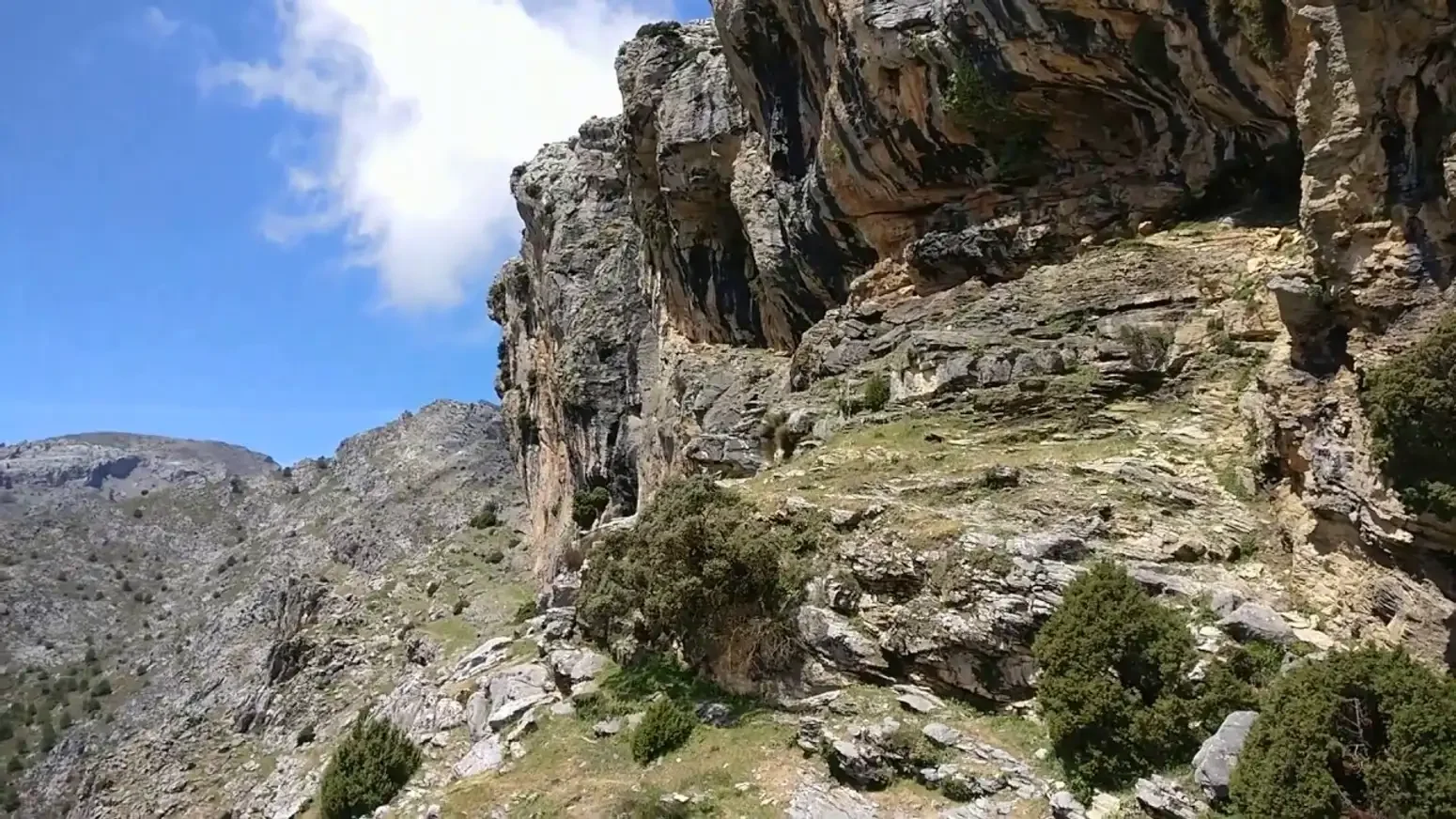 Montañas rocosas con vegetación dispersa y un cielo azul con algunas nubes.