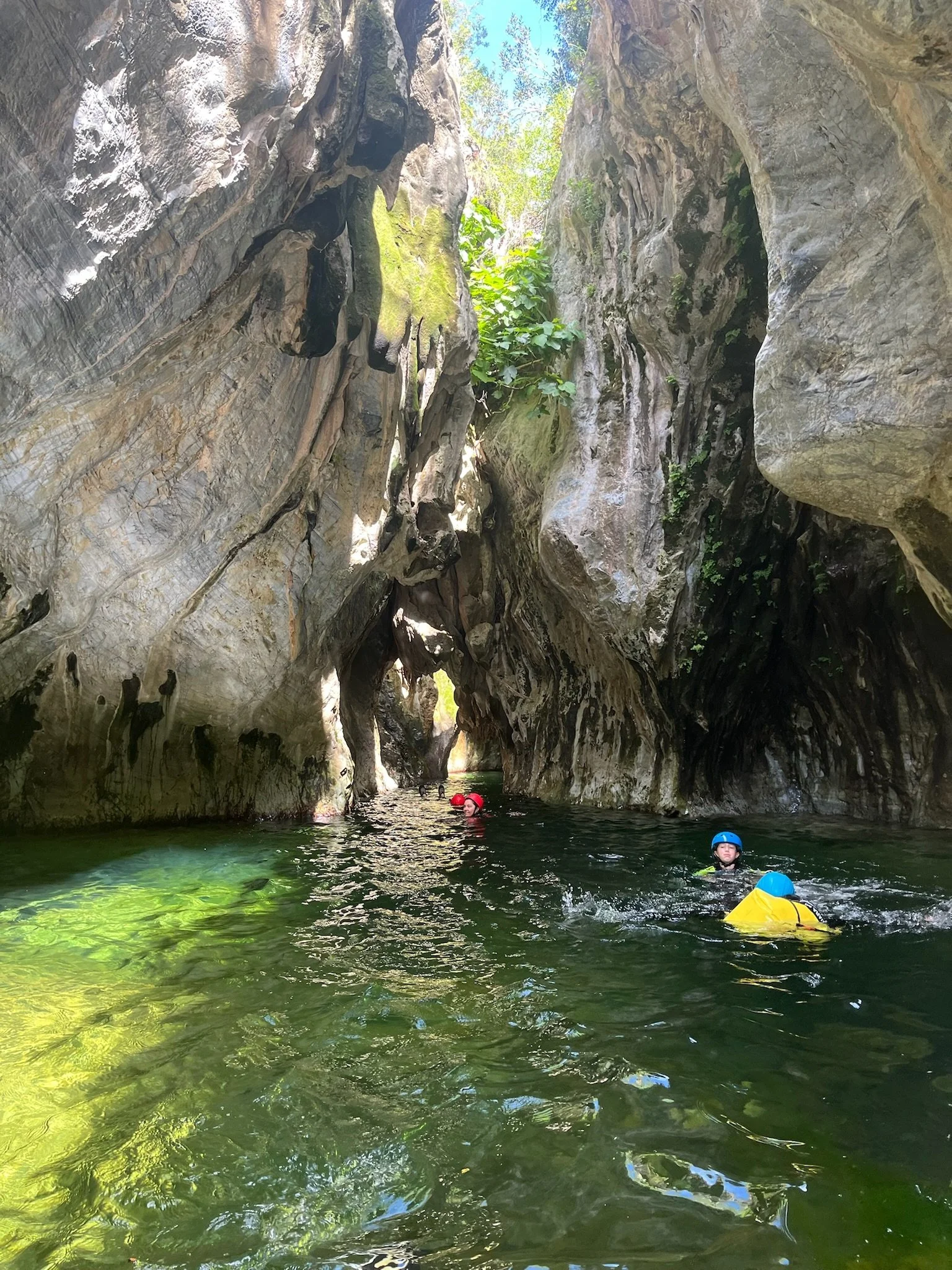Personas practicando kayaking en un río rodeado de altos acantilados de roca con vegetación en la parte superior