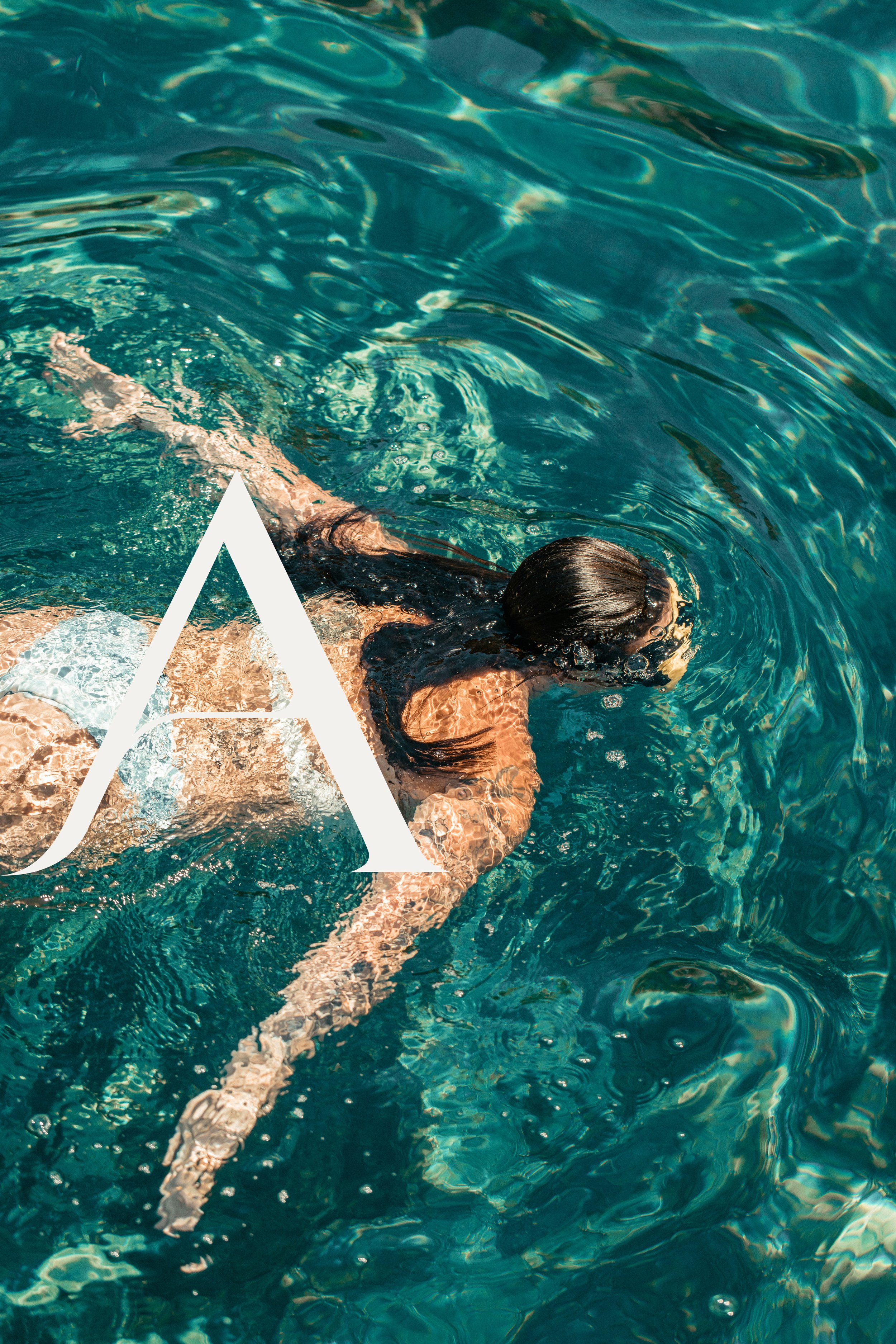 A person swimming in a body of water, with their head and arms visible, creating ripples on the water's surface.