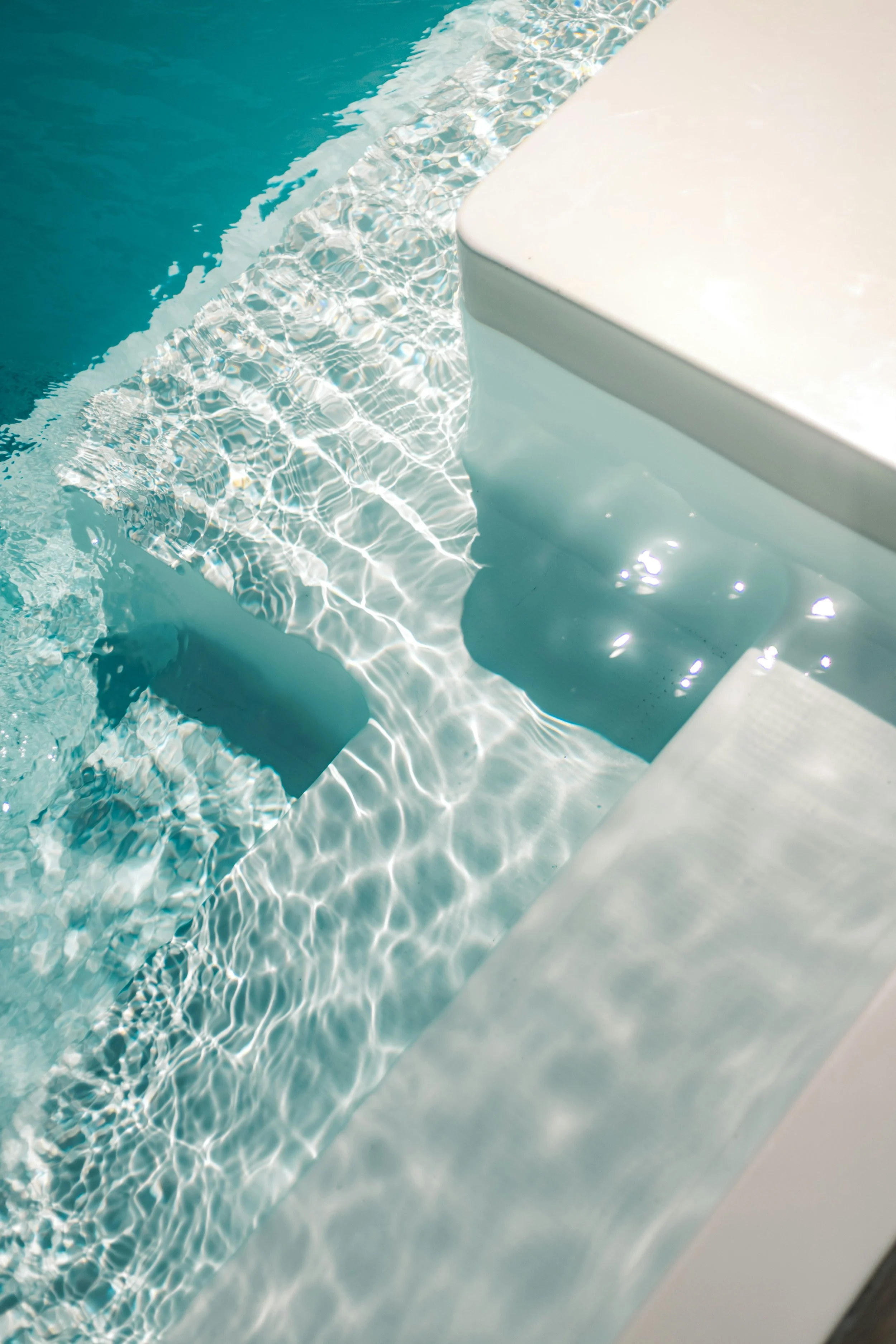 Close-up of the edge of a swimming pool, showing clear water and reflections of light.