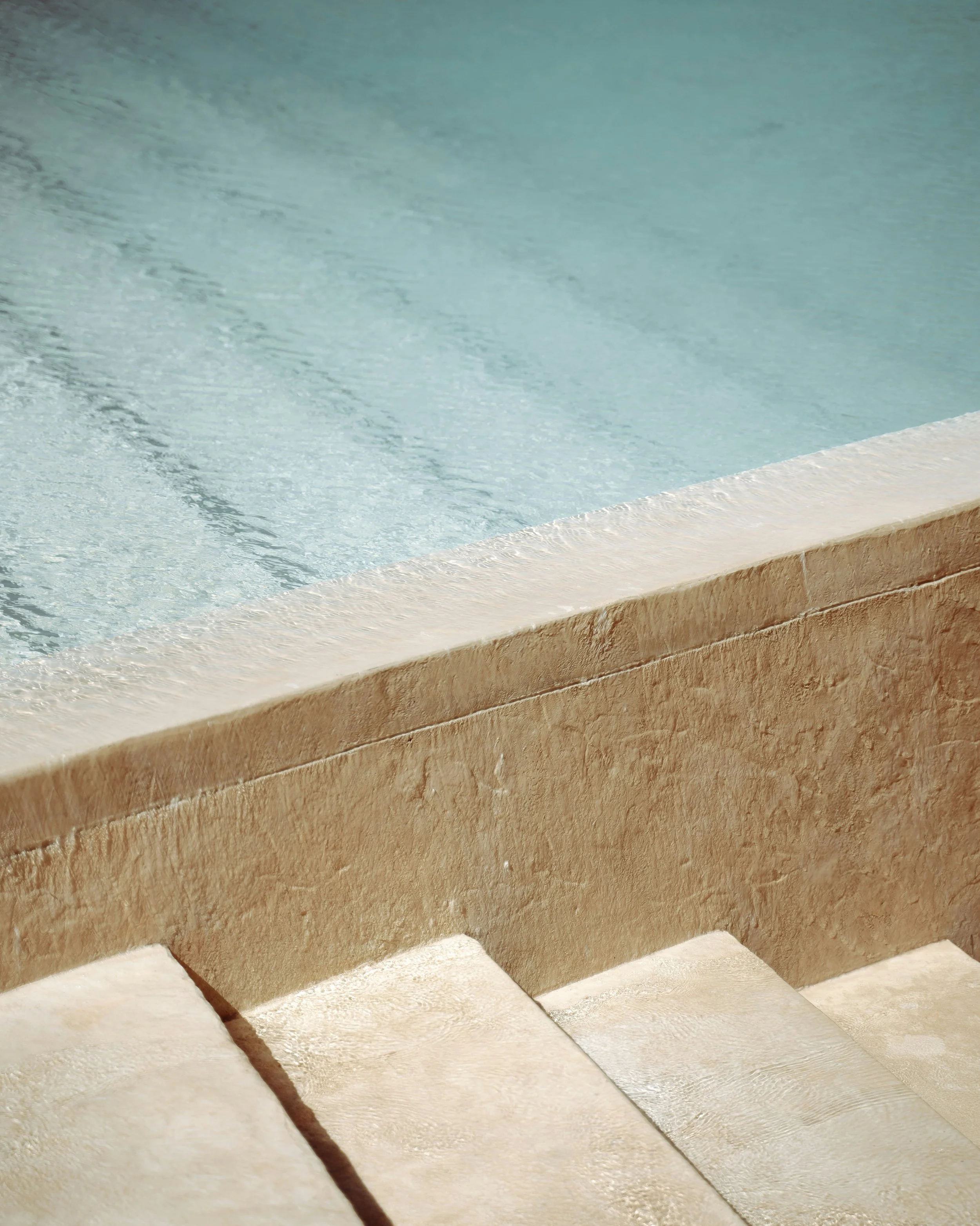 Close-up of stone steps with textured surface, leading upwards, with a rough beige stone wall on the right side.