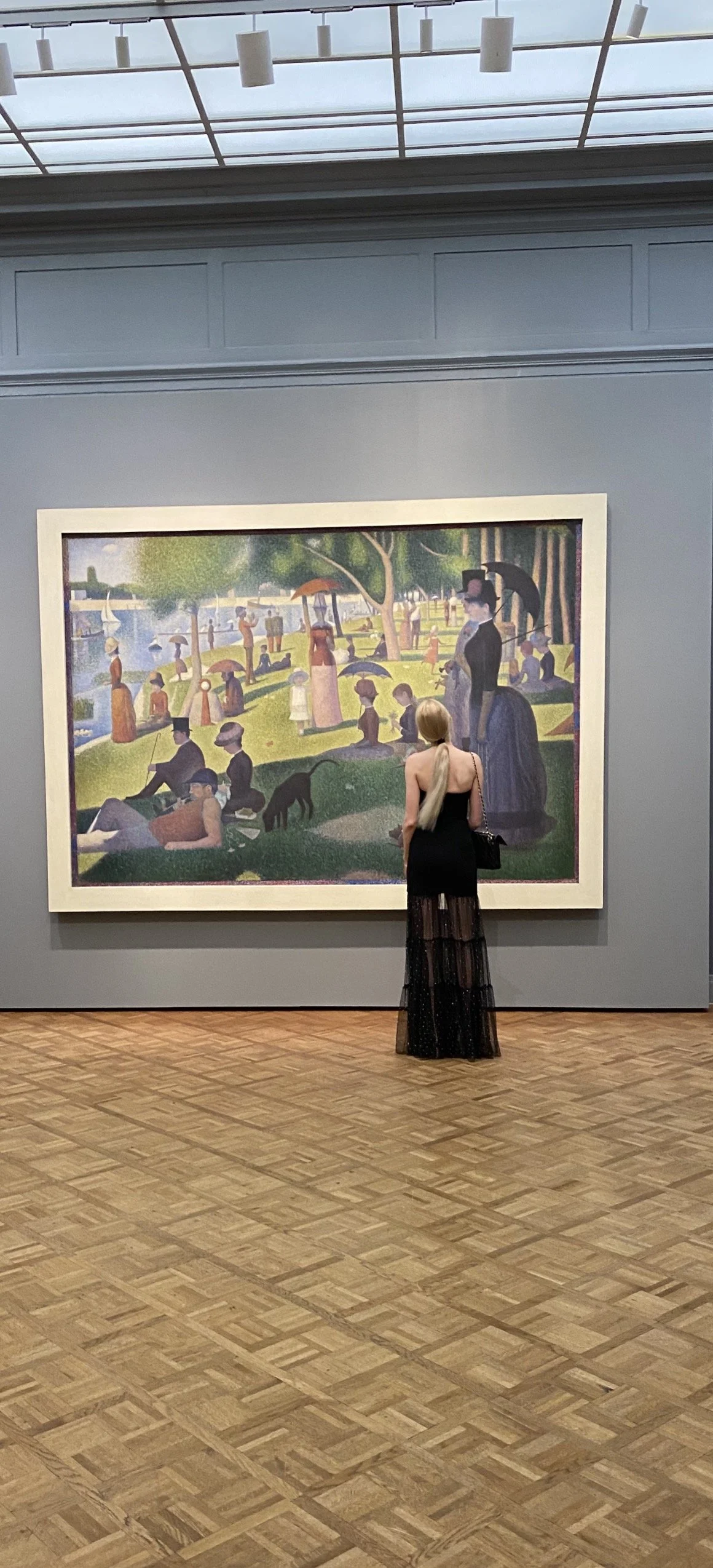Woman in a black dress viewing a pointillist painting in the Art Institute of Chicago.