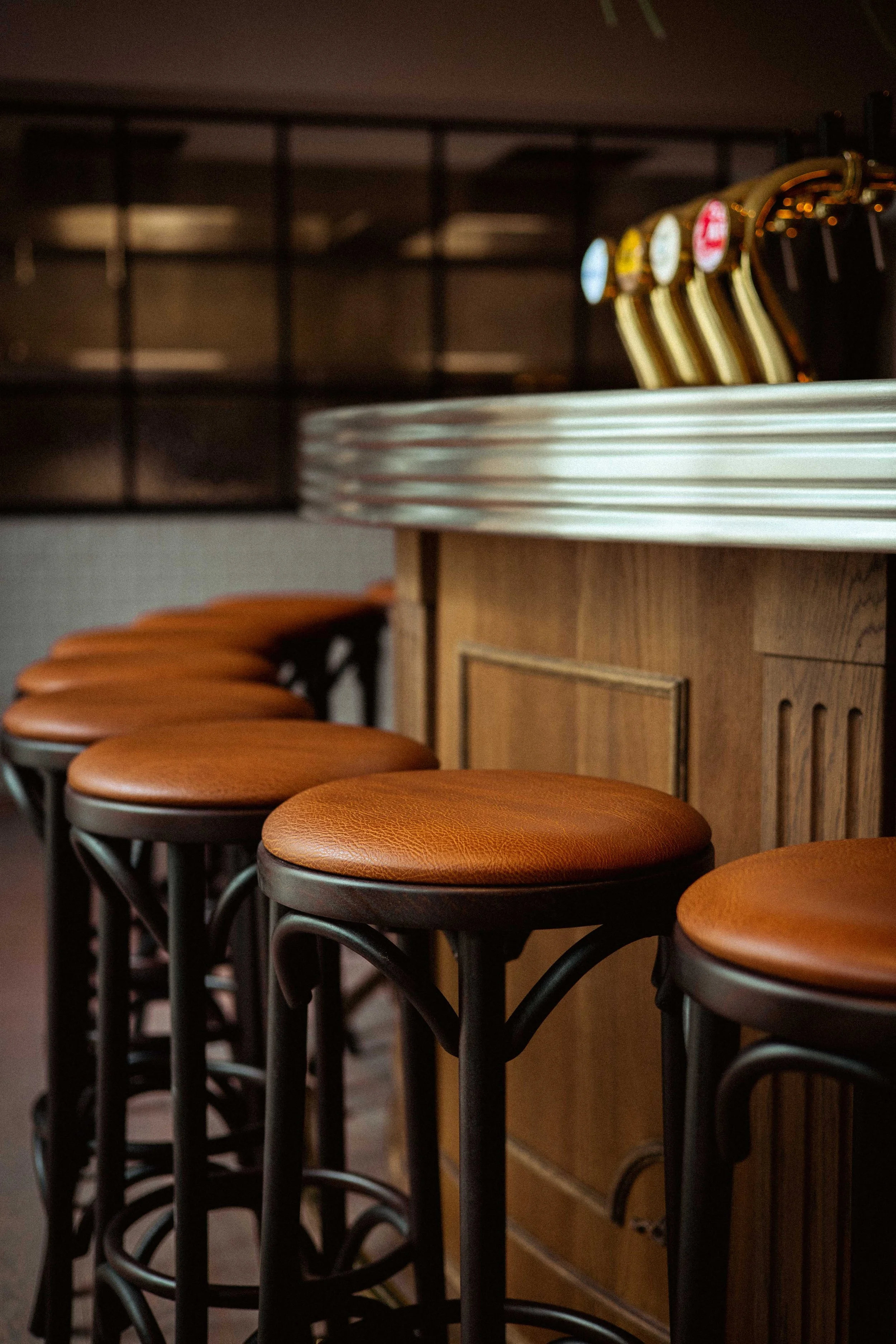 Rijen barkrukken met leren zittingen langs een houten bar in een café of restaurant.