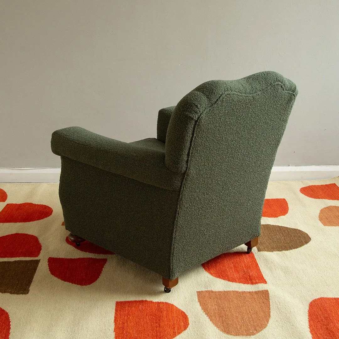 Green upholstered armchair on a patterned cream and orange rug against a plain wall.