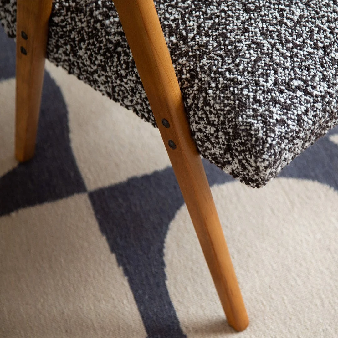 Close-up of a chair with a black and white boucle fabric seat and wooden legs on a geometric patterned carpet.