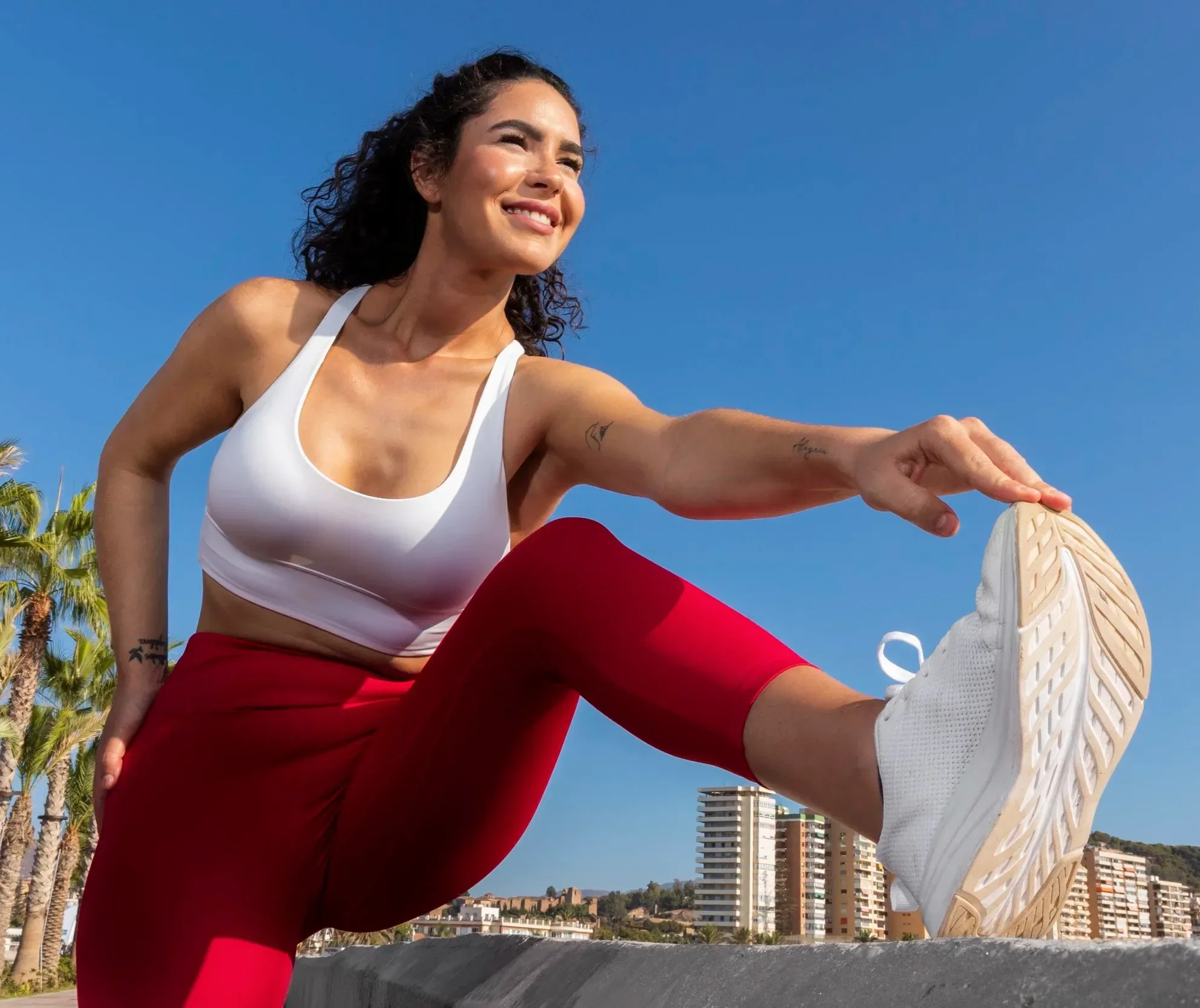 Woman in workout clothes doing a yoga pose outdoors with a cityscape and blue sky in the background.