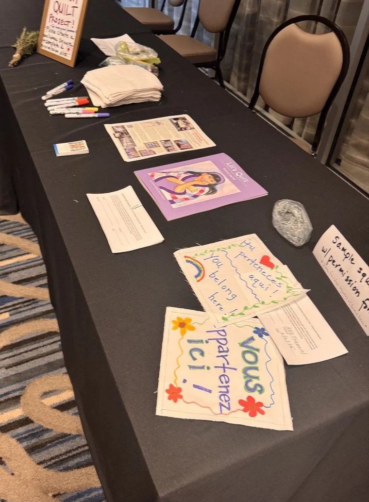 A table with handmade signs, markers, pamphlets, and a clear rock, possibly at an event or community fair.