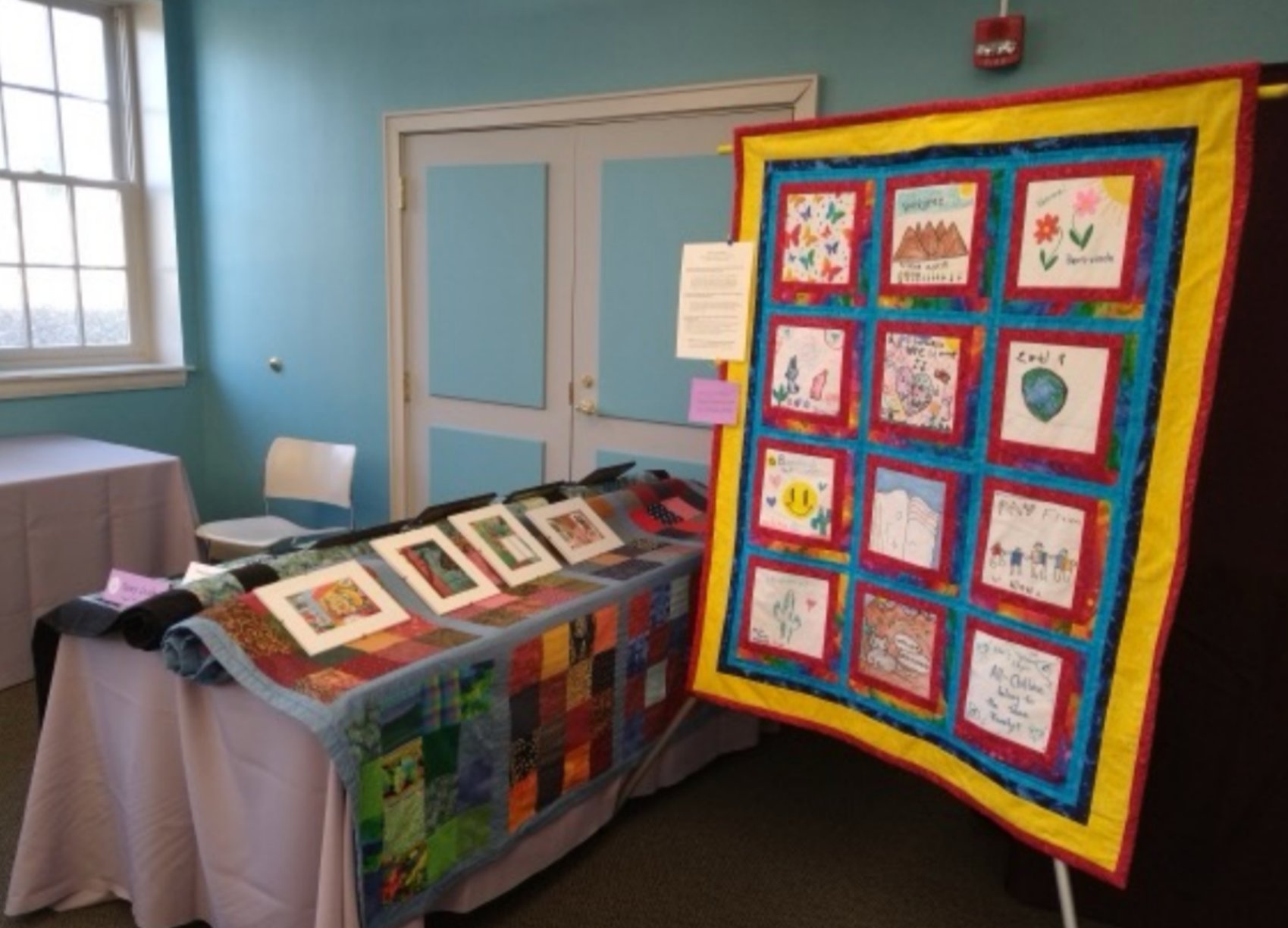 Display of handmade quilts and artwork at an indoor exhibit.